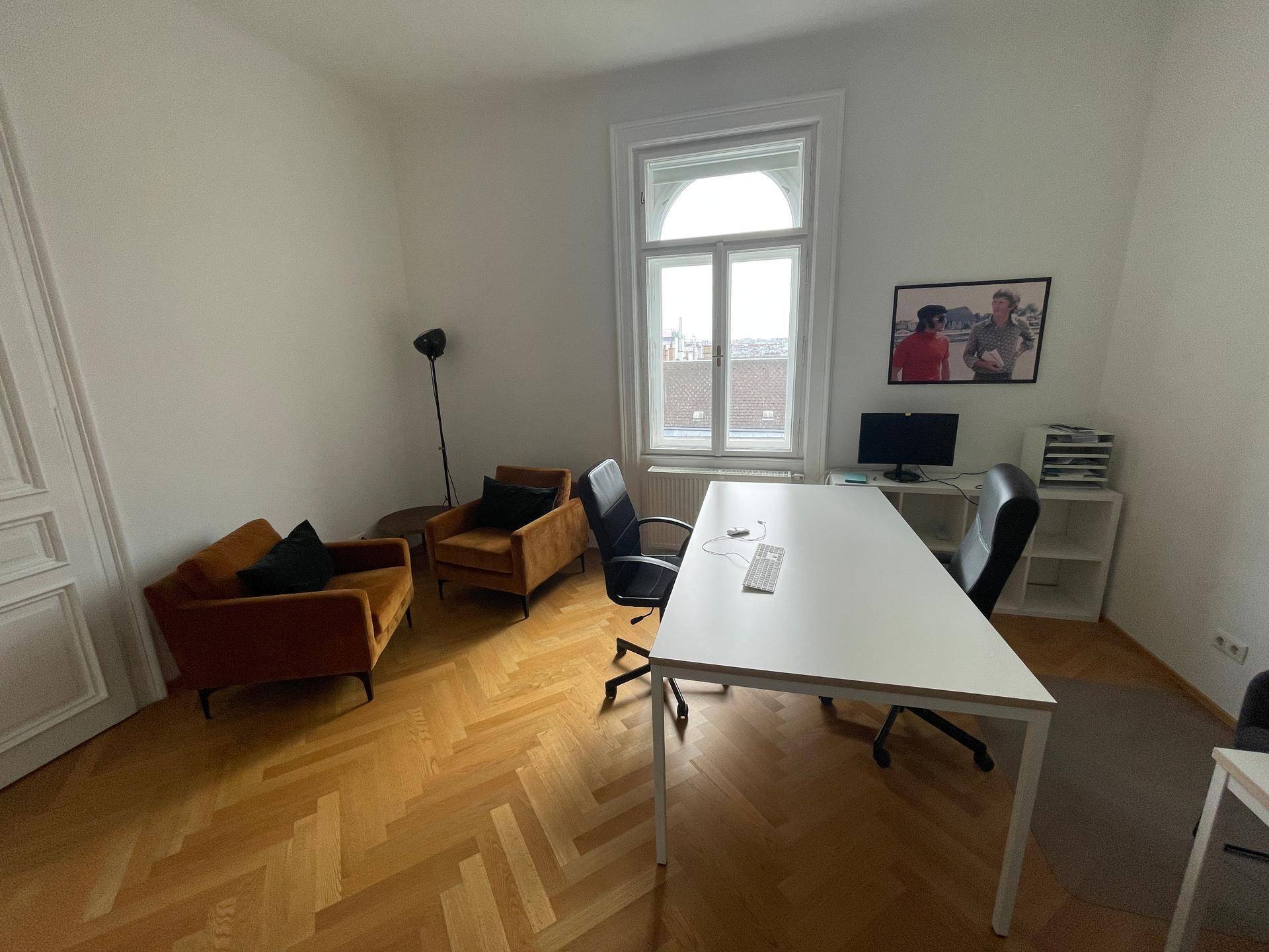 Büro mit zwei bequemen Sesseln, einem Schreibtisch und einem großen Fenster, das viel Tageslicht hereinlässt.