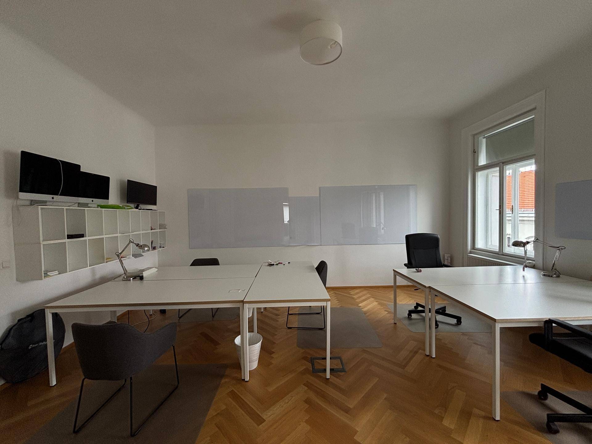 Modernes Büro mit mehreren Arbeitsplätzen, weißen Schreibtischen und praktischen Regalen an der Wand.