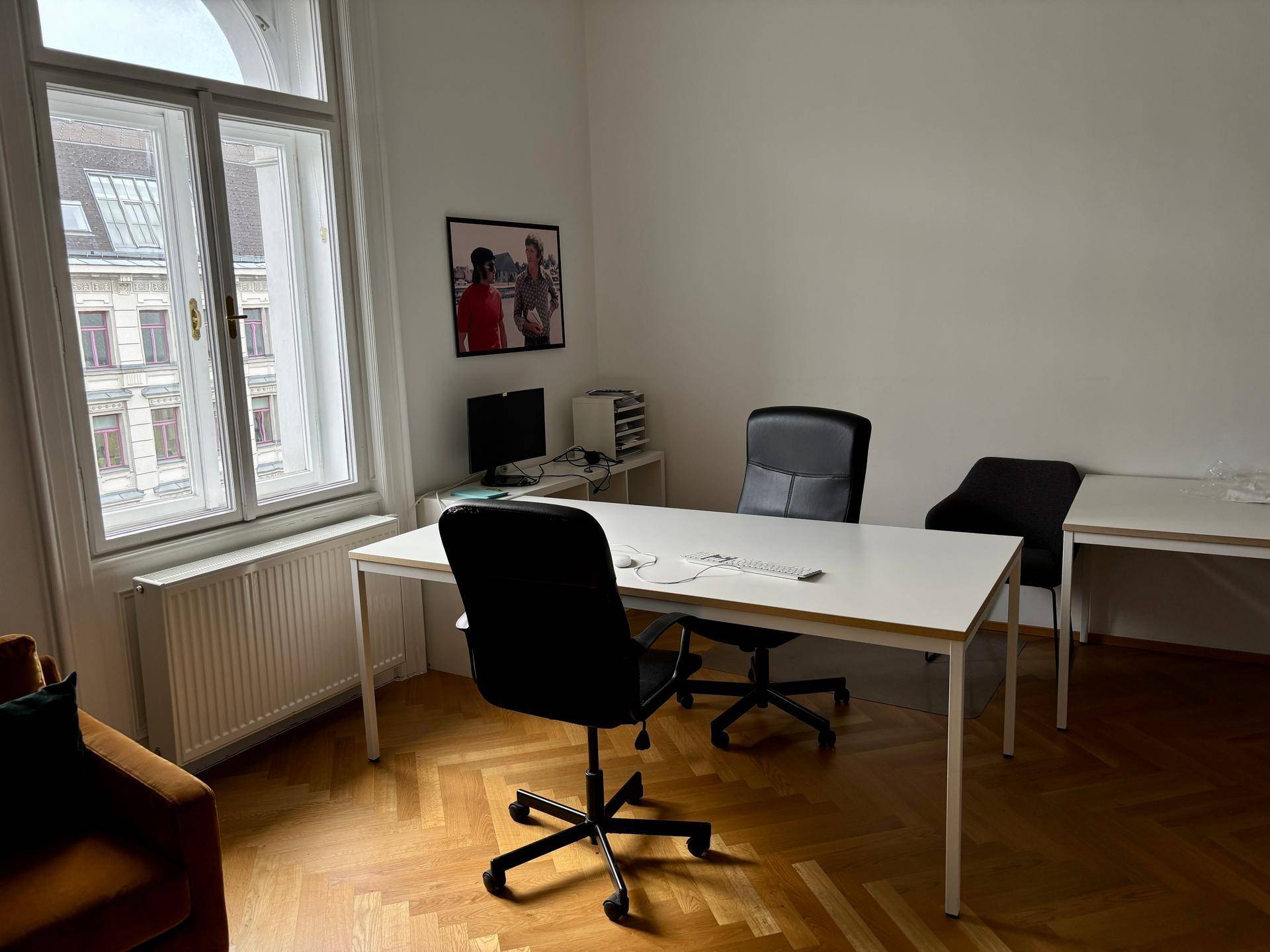 Helles Büro mit einem Schreibtisch, Bürostühlen und einem großen Fenster mit Heizkörper für Komfort.