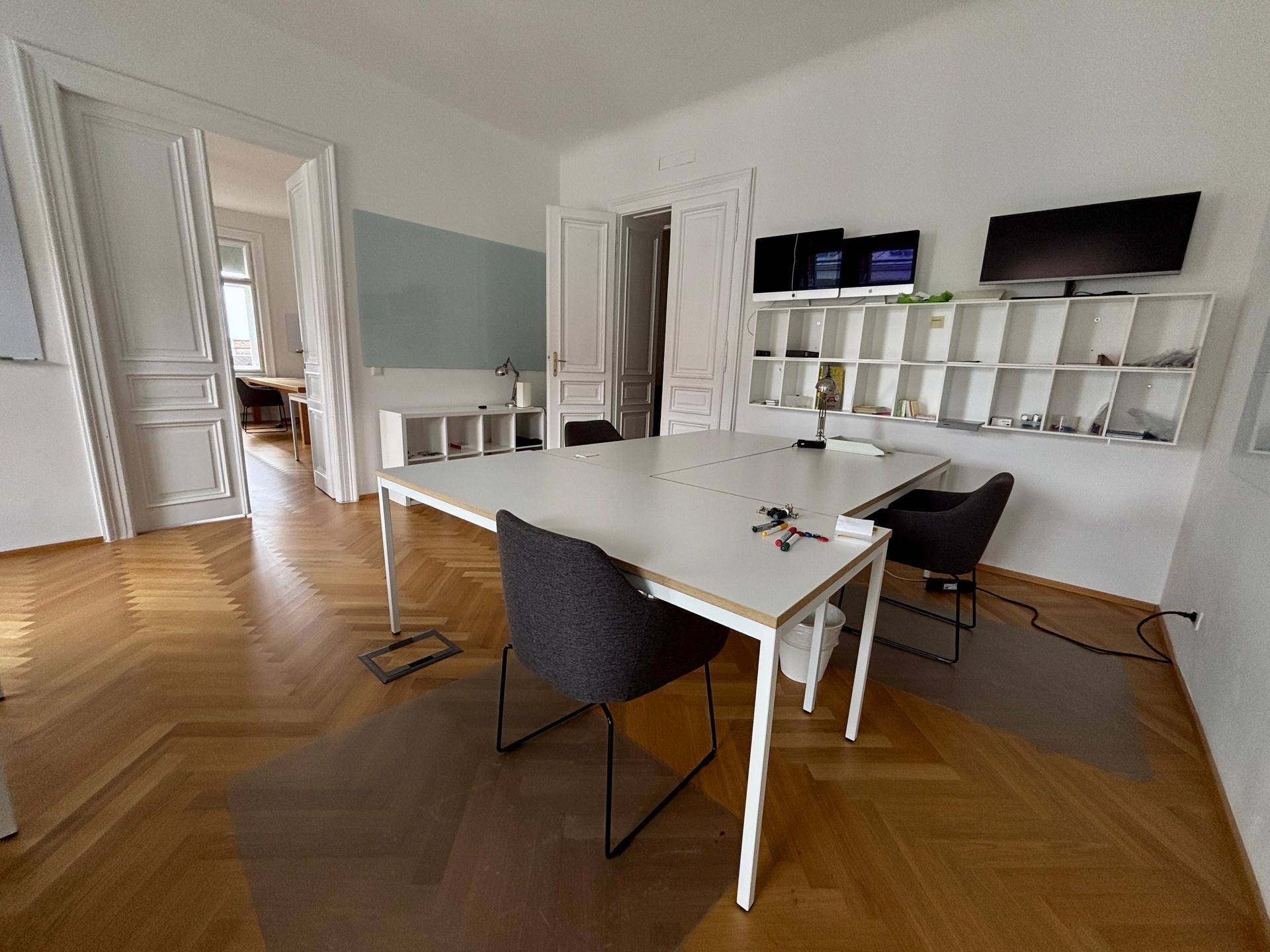 Geräumiges Büro mit einem großen Besprechungstisch, Stühlen und Wandregalen für eine organisierte Arbeitsfläche.