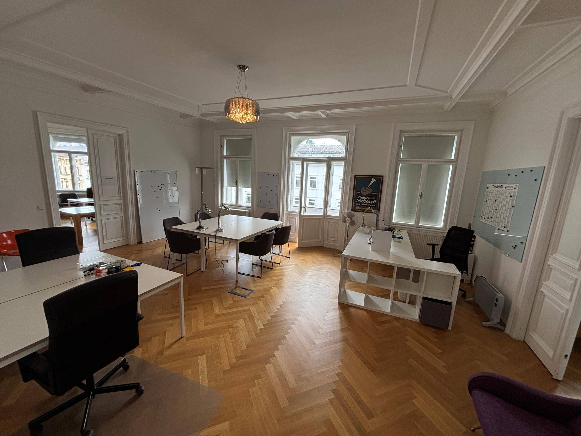 Geräumiges Büro mit mehreren Arbeitsplätzen, hohen Decken und Fischgrätparkett, ideal für ein Team.