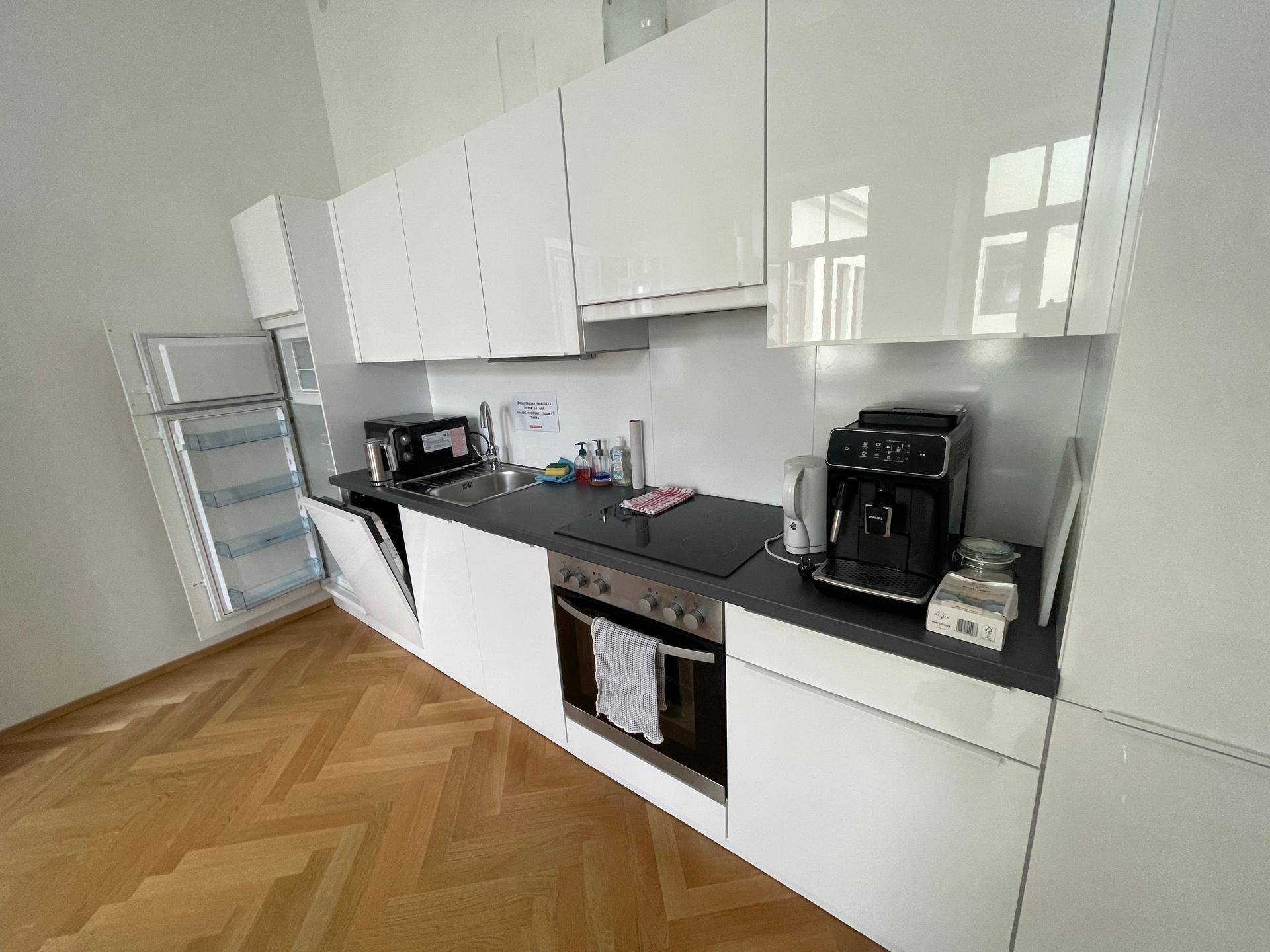 Moderne Einbauküche mit weißen Hochglanzschränken, Spülmaschine, Ofen und Kaffeemaschine.