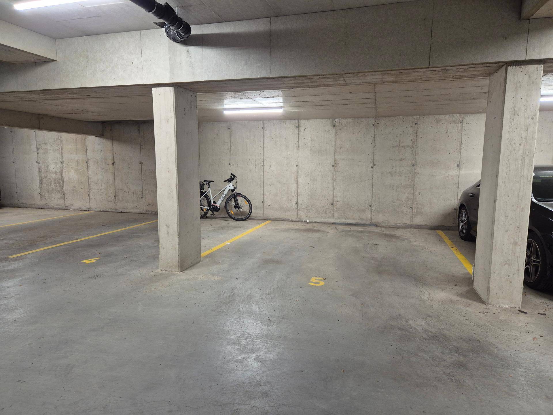 Tiefgaragenstellplatz mit Betonboden und markierten Parkflächen, inklusive Fahrradabstellmöglichkeit.