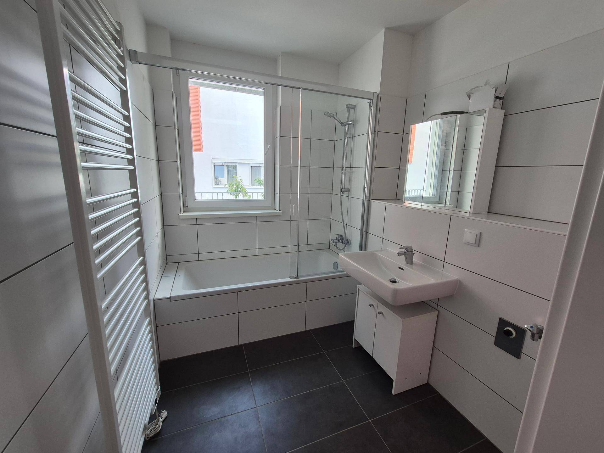 Modernes Badezimmer mit Badewanne, Duschabtrennung, Fenster und einem praktischen Handtuchheizkörper.