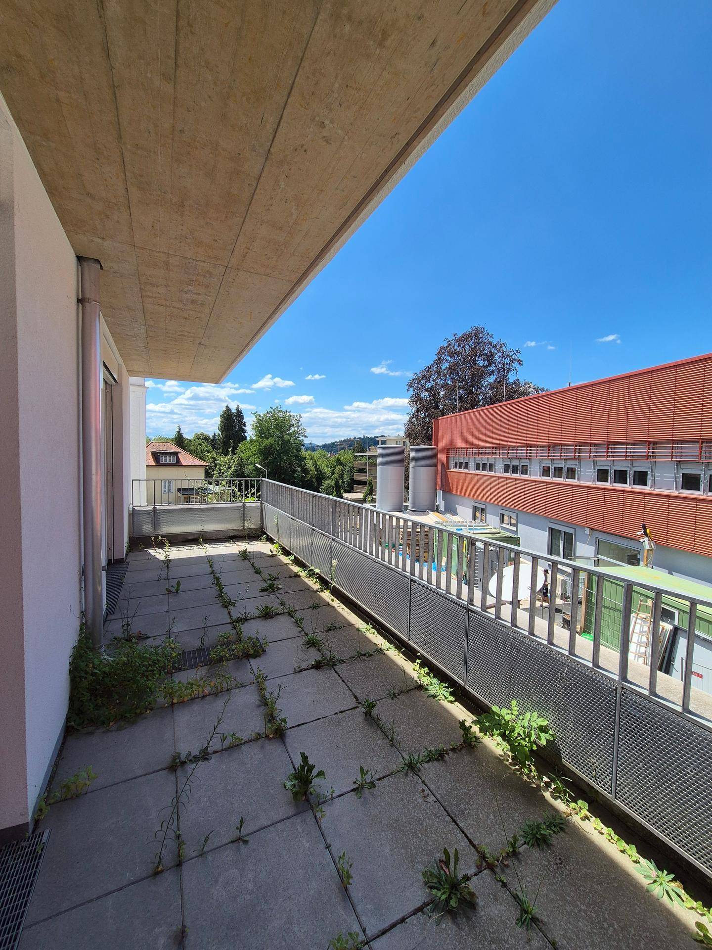 Großer Balkon mit Fliesenboden und Blick auf die grüne Umgebung unter blauem Himmel.