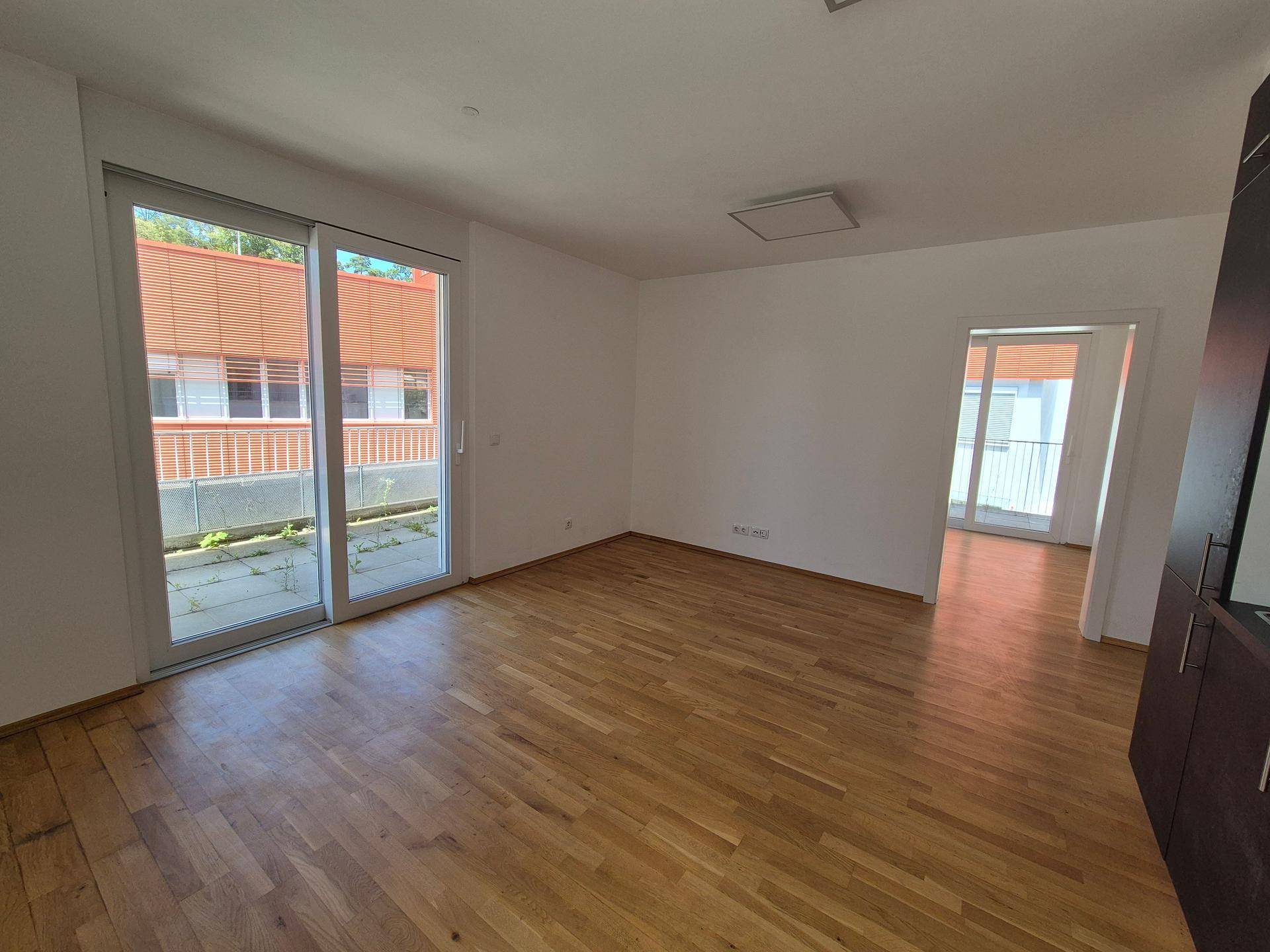 Geräumiges Zimmer mit Holzboden, großen Schiebetüren und offenem Durchgang zu einem weiteren Raum.