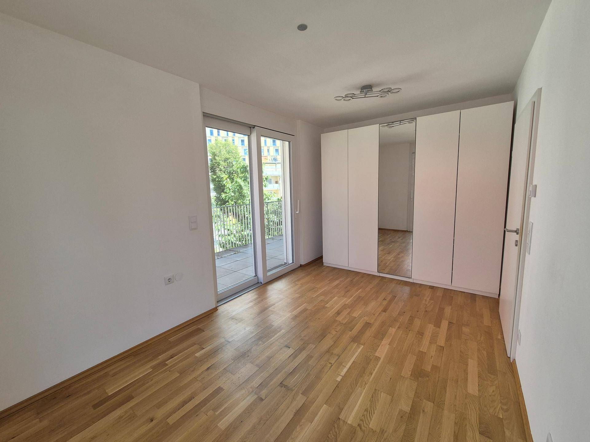 Helles Schlafzimmer mit Parkettboden und einem großen, weißen Einbauschrank mit Spiegeltüren.