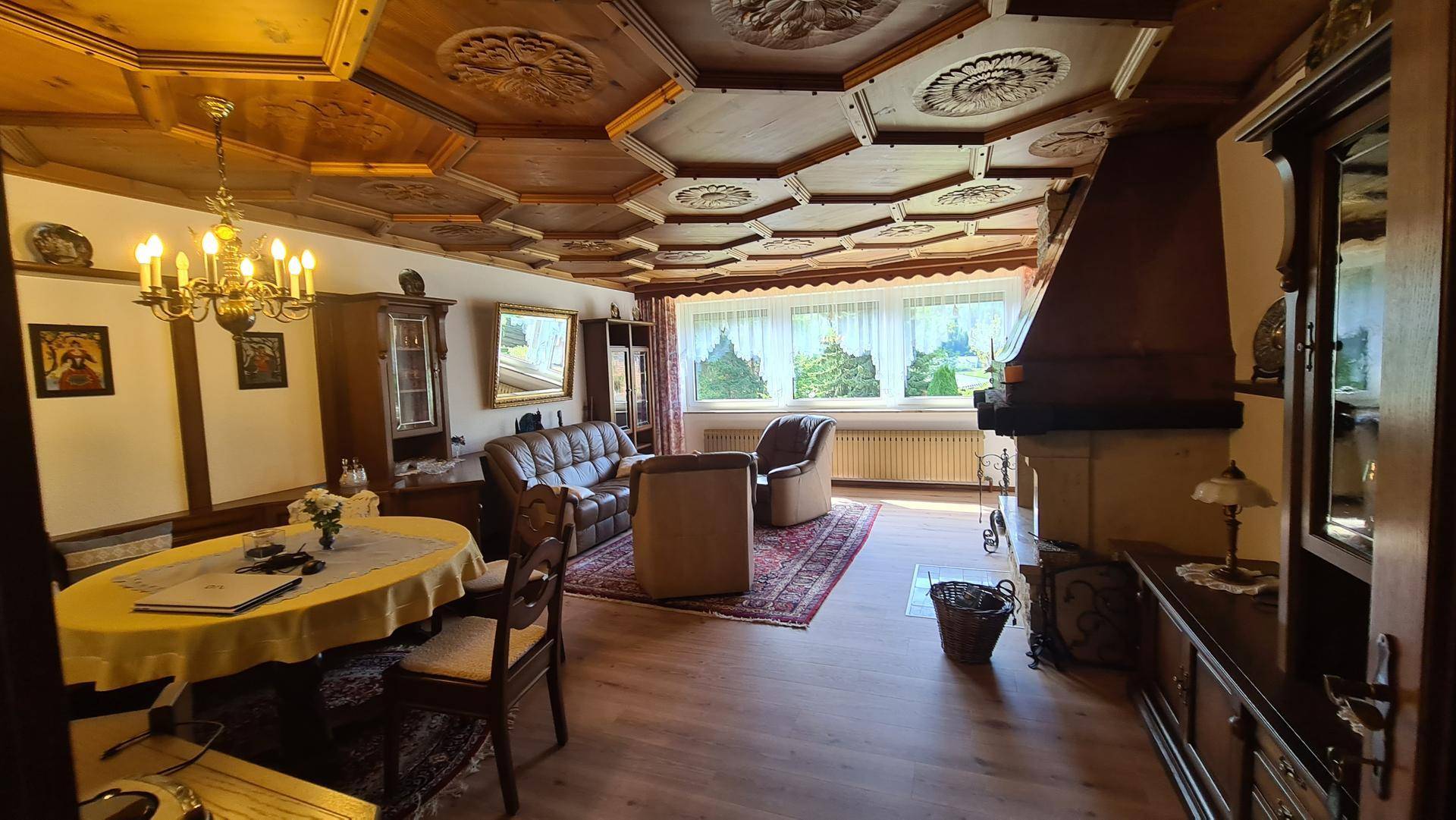 Gemütlicher Wohn- und Essbereich mit kunstvoll geschnitzter Holzdecke und traditionellem Kamin.