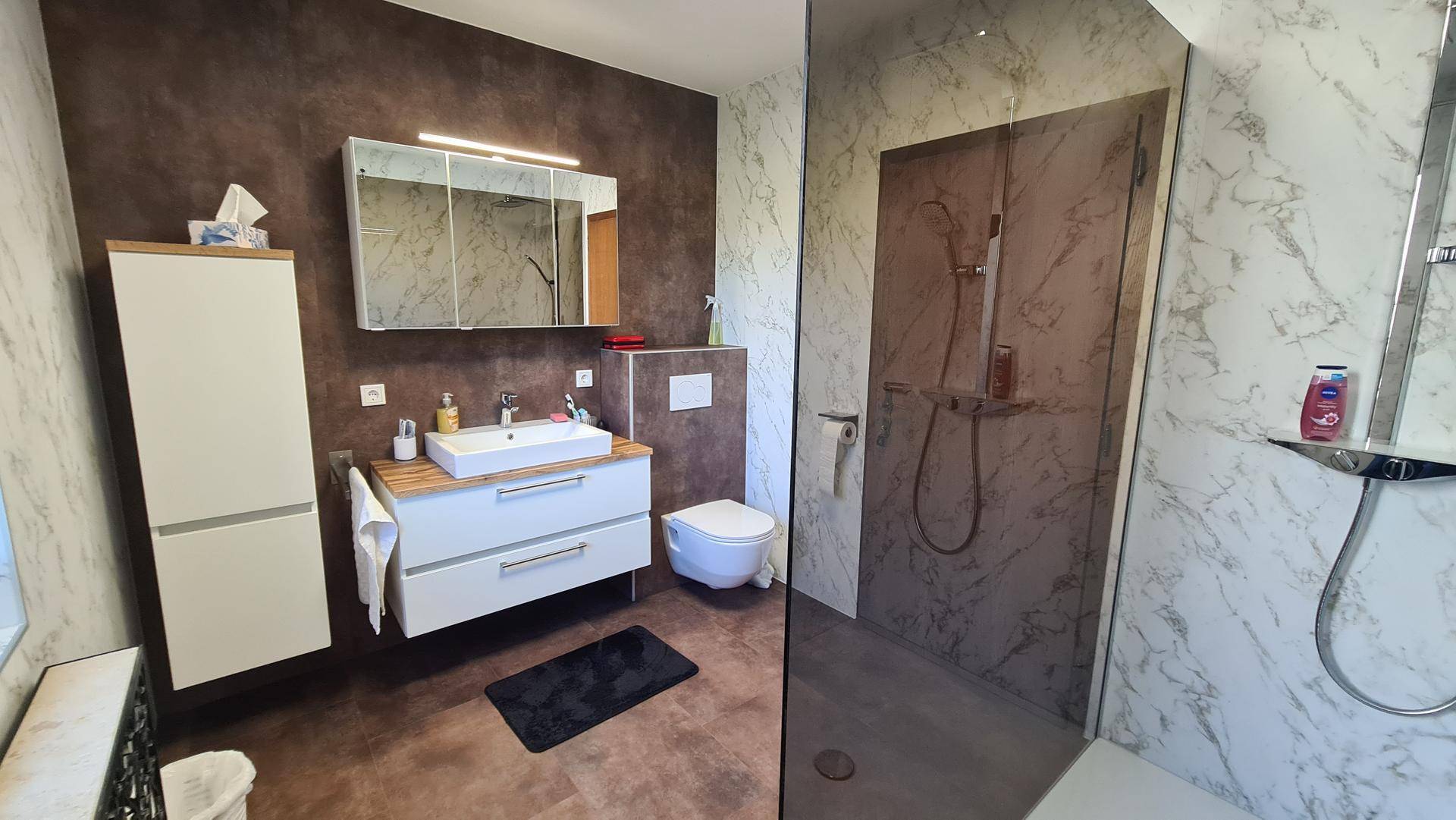 Modernes Badezimmer mit begehbarer Dusche, Wand-WC und eleganten Marmor-Effekt-Fliesen.