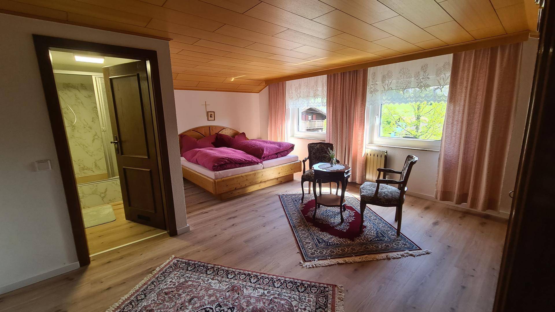 Helles Schlafzimmer mit Holzbett, traditionellen Möbeln und Blick ins Grüne, mit Badzugang.