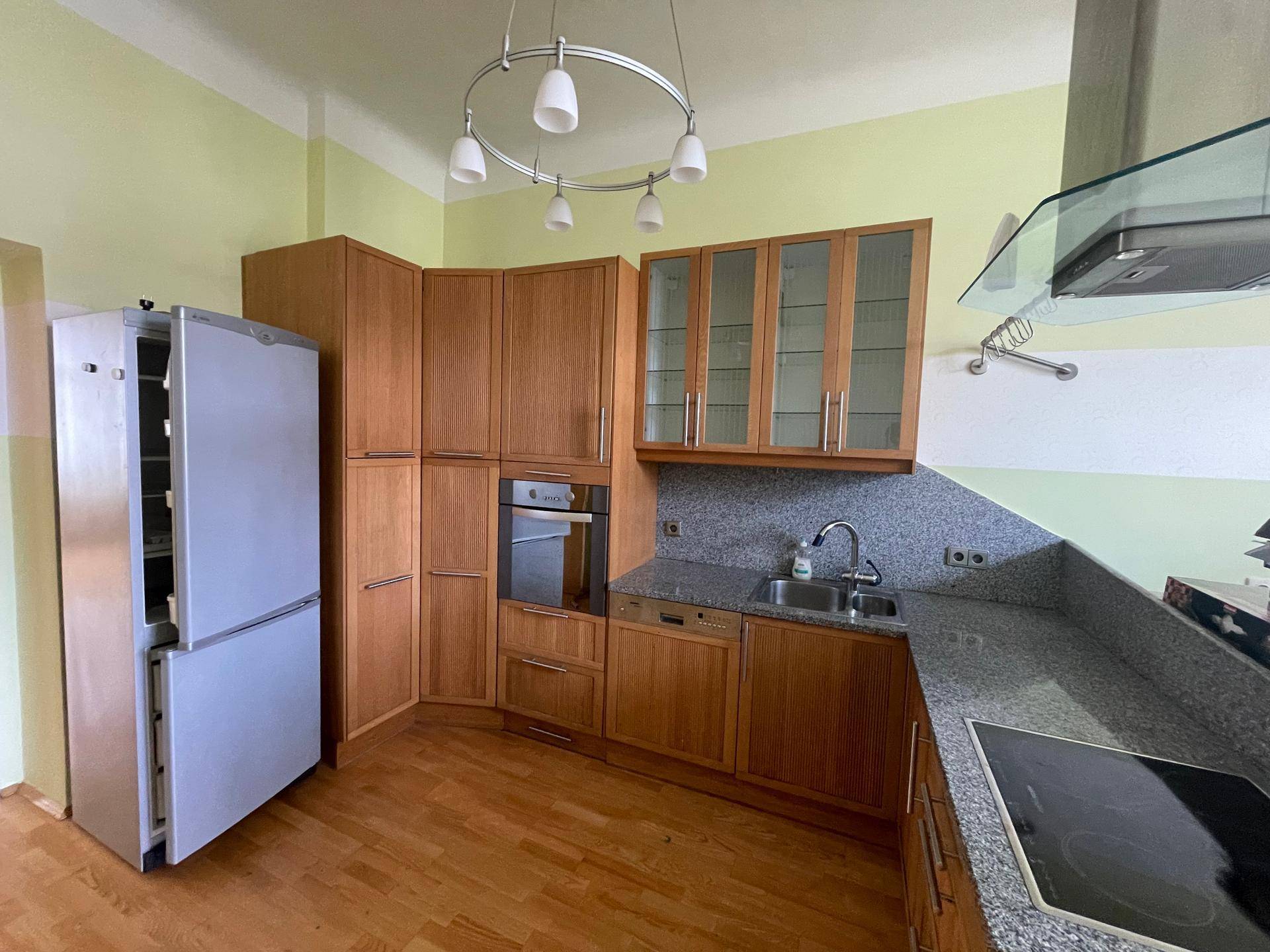 Geräumige Küche mit Holzfronten, Granitarbeitsplatten, Kühlschrank und Induktionskochfeld.