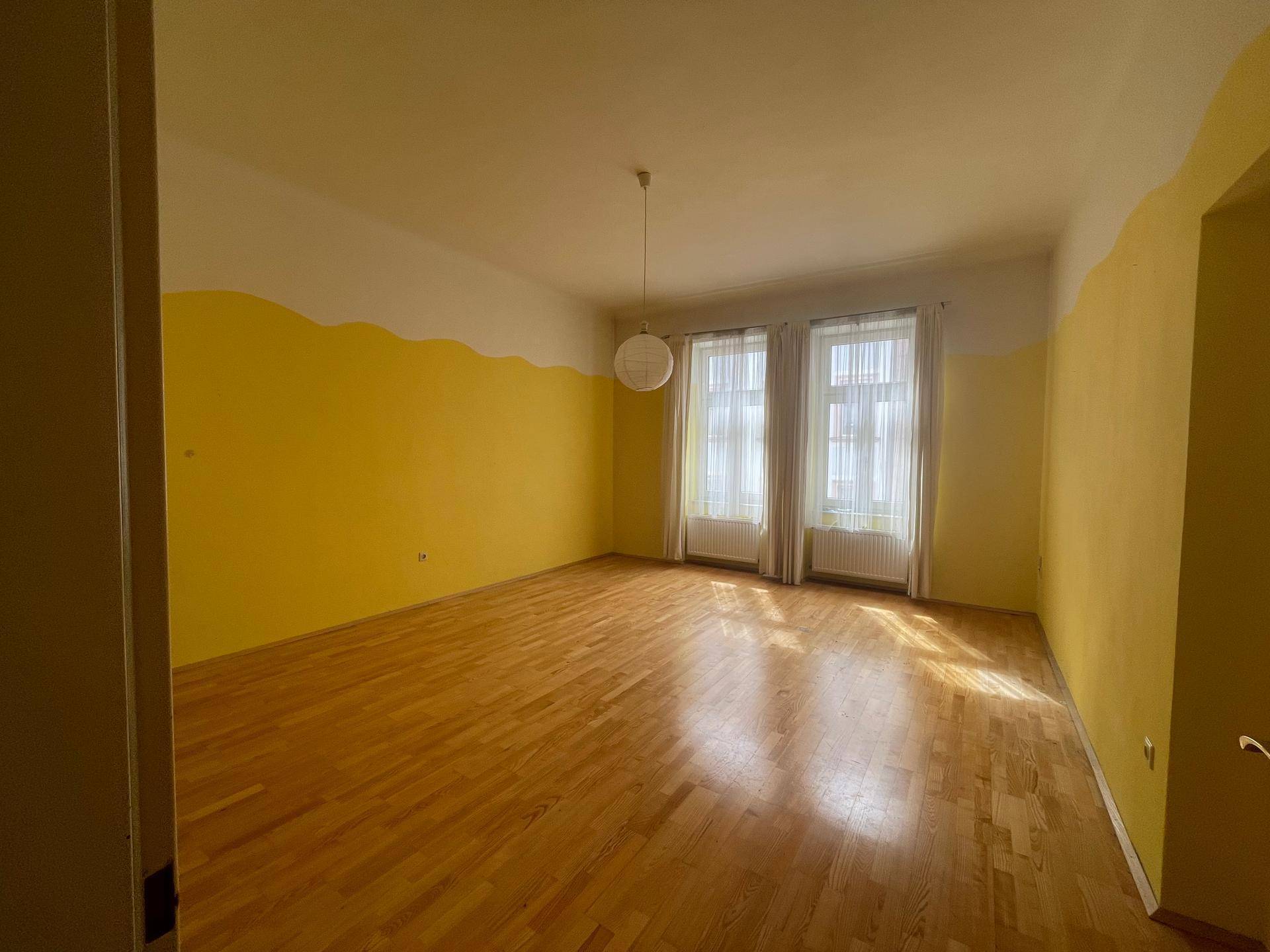 Großes, helles Zimmer mit gelb-weißen Wänden und Holzboden, ideal als Wohn- oder Schlafzimmer.