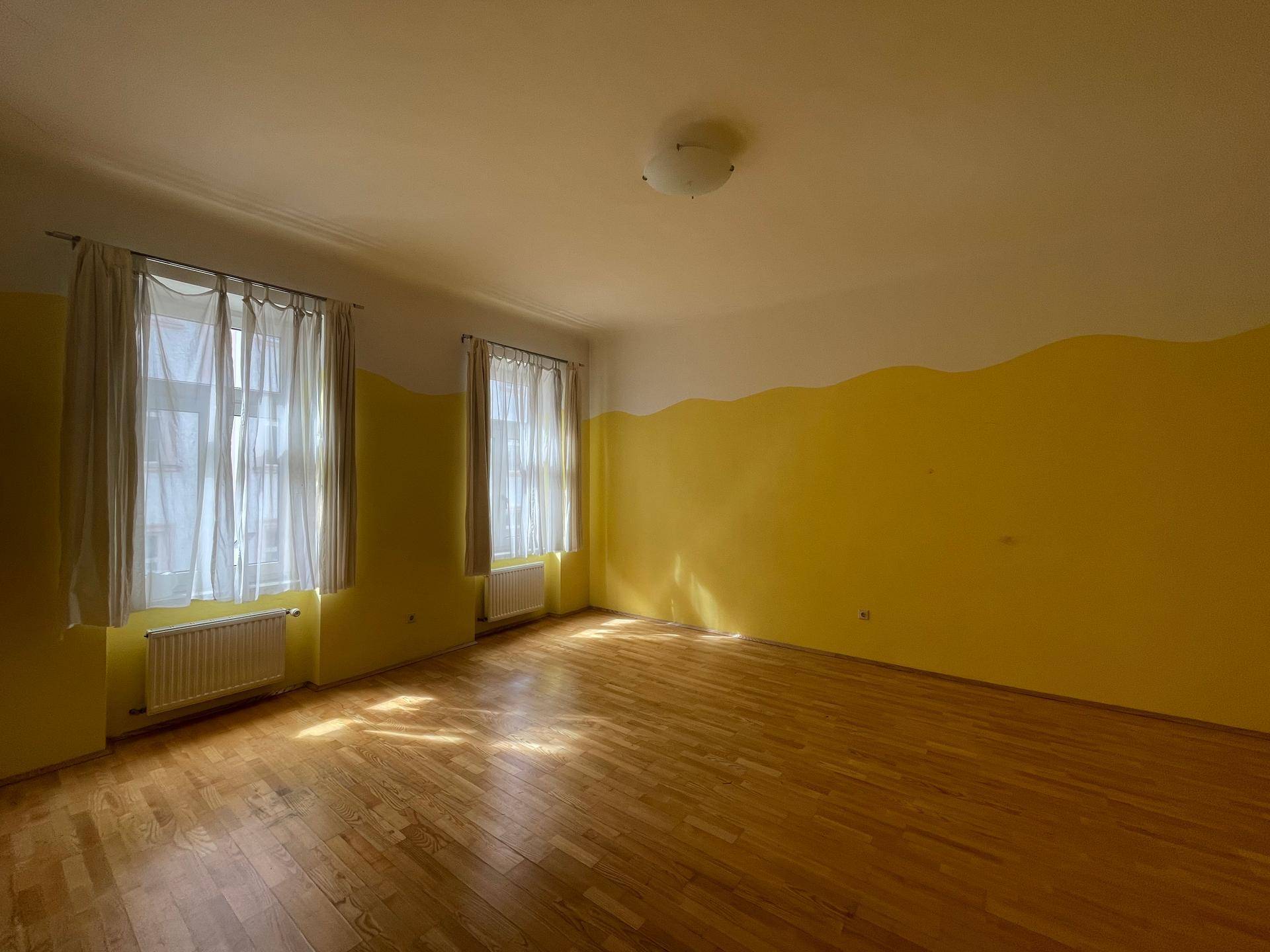 Helles Zimmer mit gelb-weißen Wänden und Holzboden, bereit zur individuellen Gestaltung.