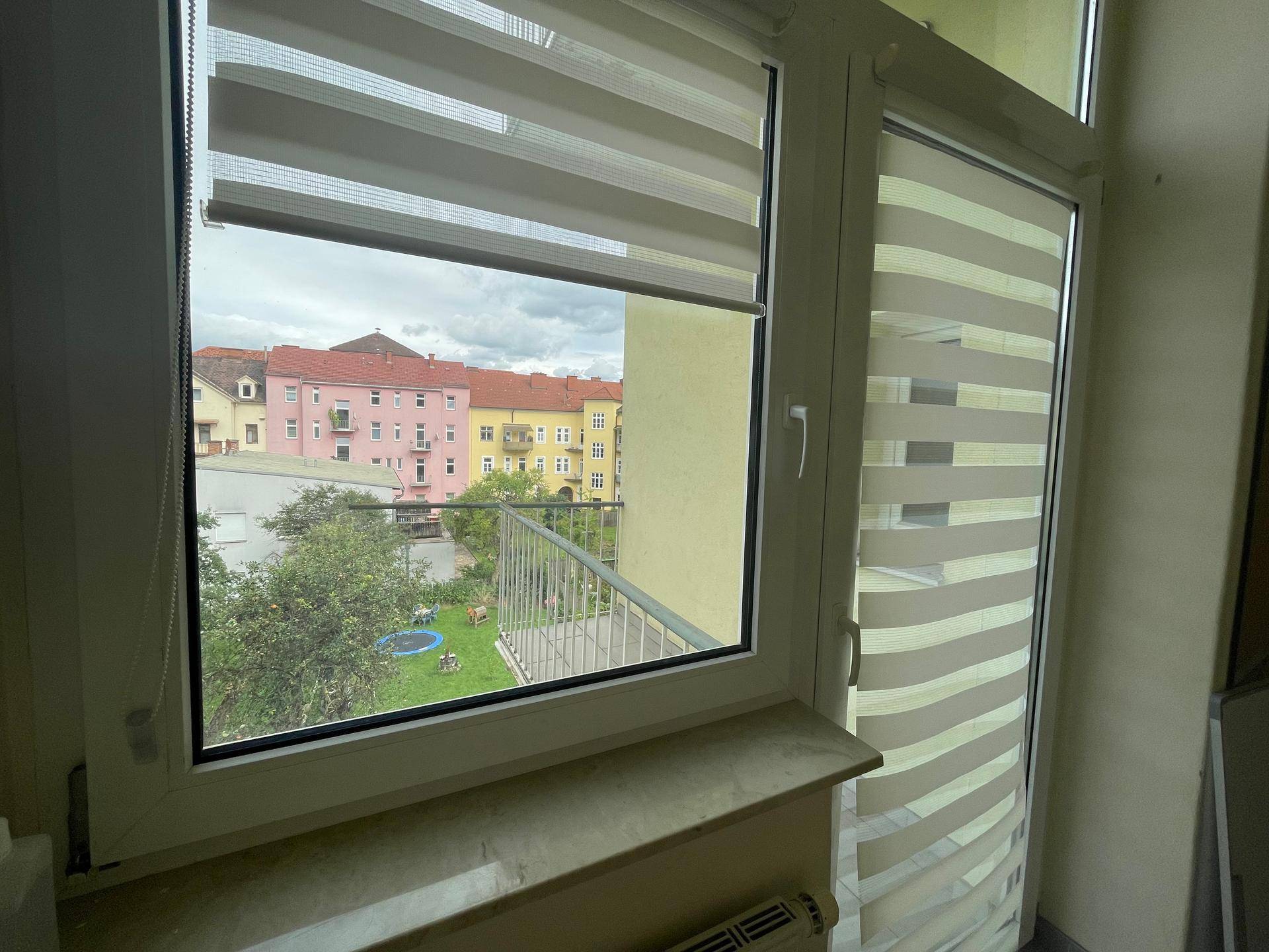 Blick vom Fenster auf den Balkon und den grünen Innenhof mit Spielbereich.