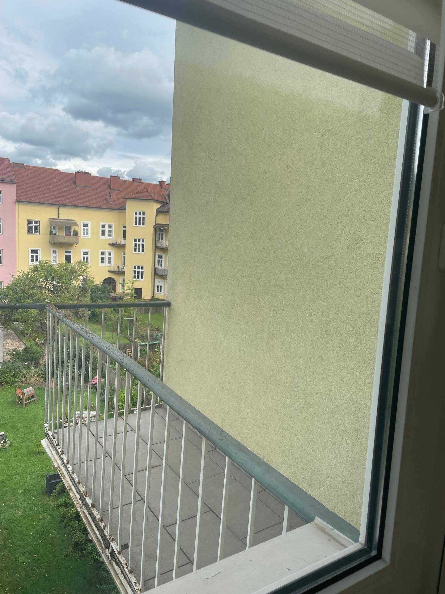Balkon mit Metallgeländer und Blick auf den grünen Innenhof und umliegende Gebäude.