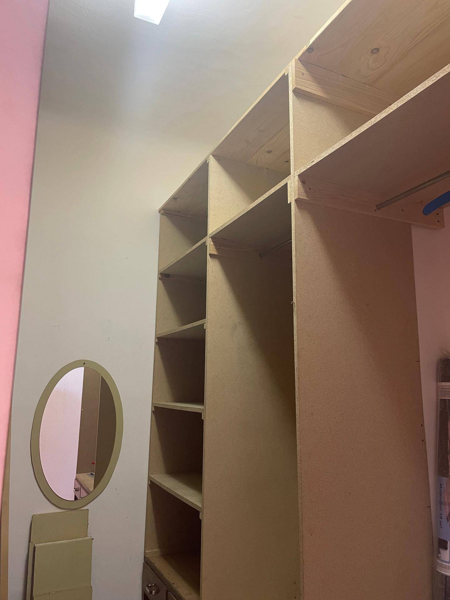 Begehbarer Schrankraum mit offenen Regalen und einem kleinen Spiegel an der Wand.