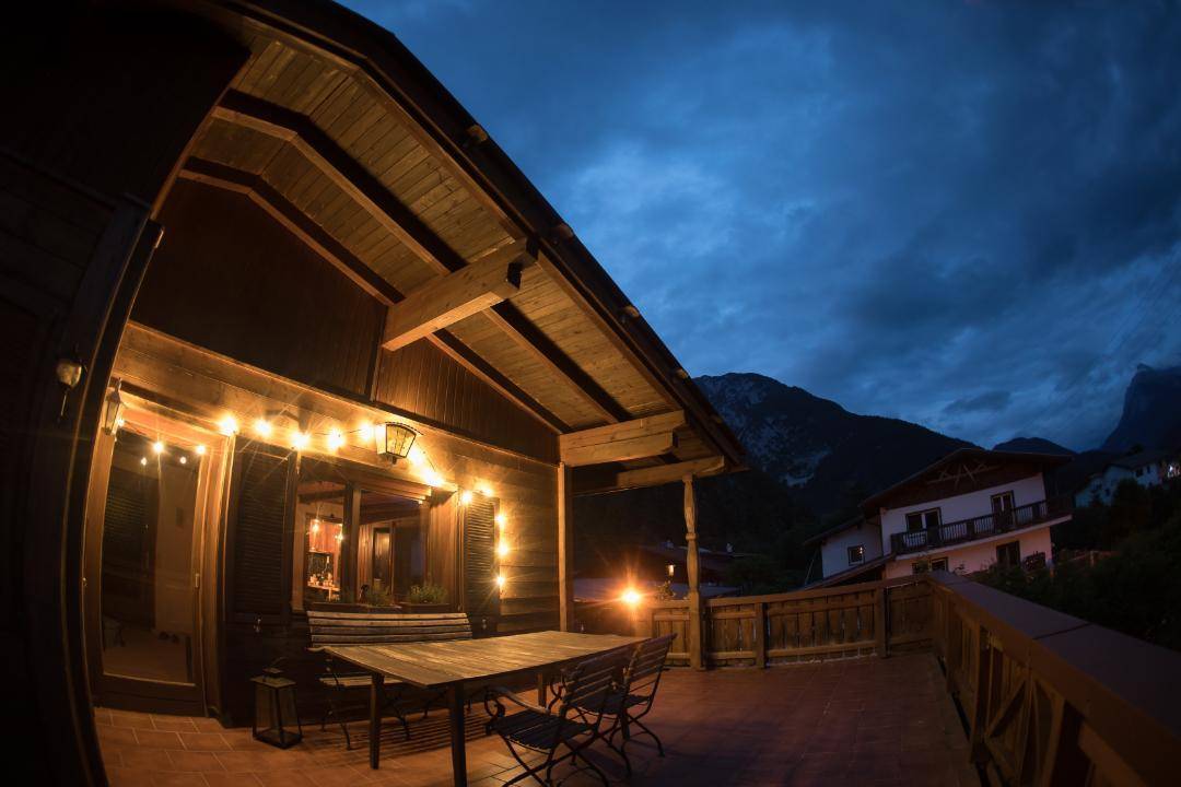 Große Terrasse am Abend mit Lichterketten, Esstisch und Bergblick unter dunklem Himmel.