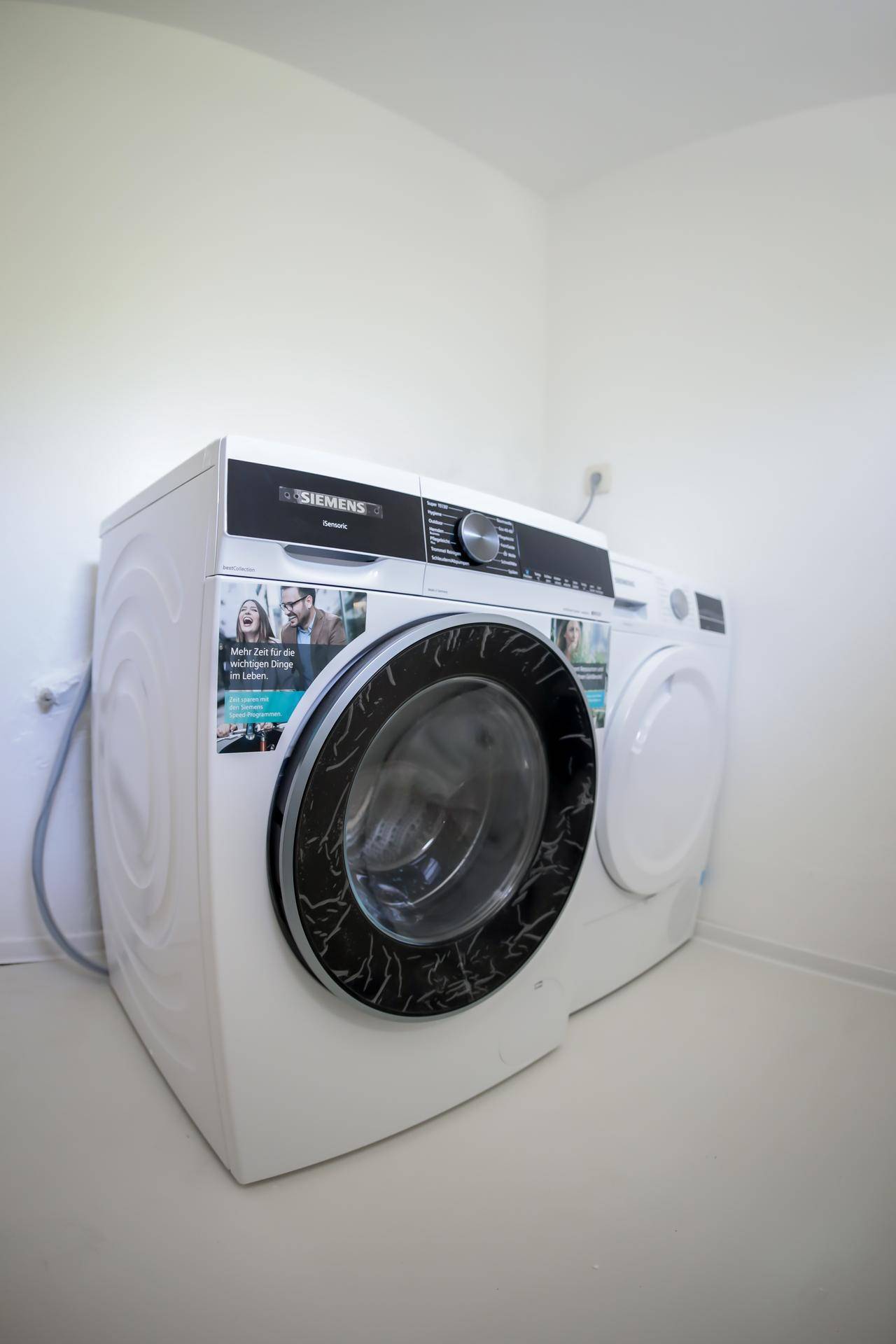 Waschküche mit moderner Siemens Waschmaschine und Trockner in hellem Raum.