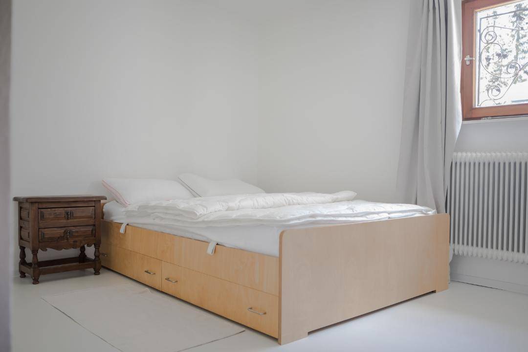 Helles Schlafzimmer mit weiß gestrichenen Wänden, Holzbett mit Stauraum und Nachttisch.