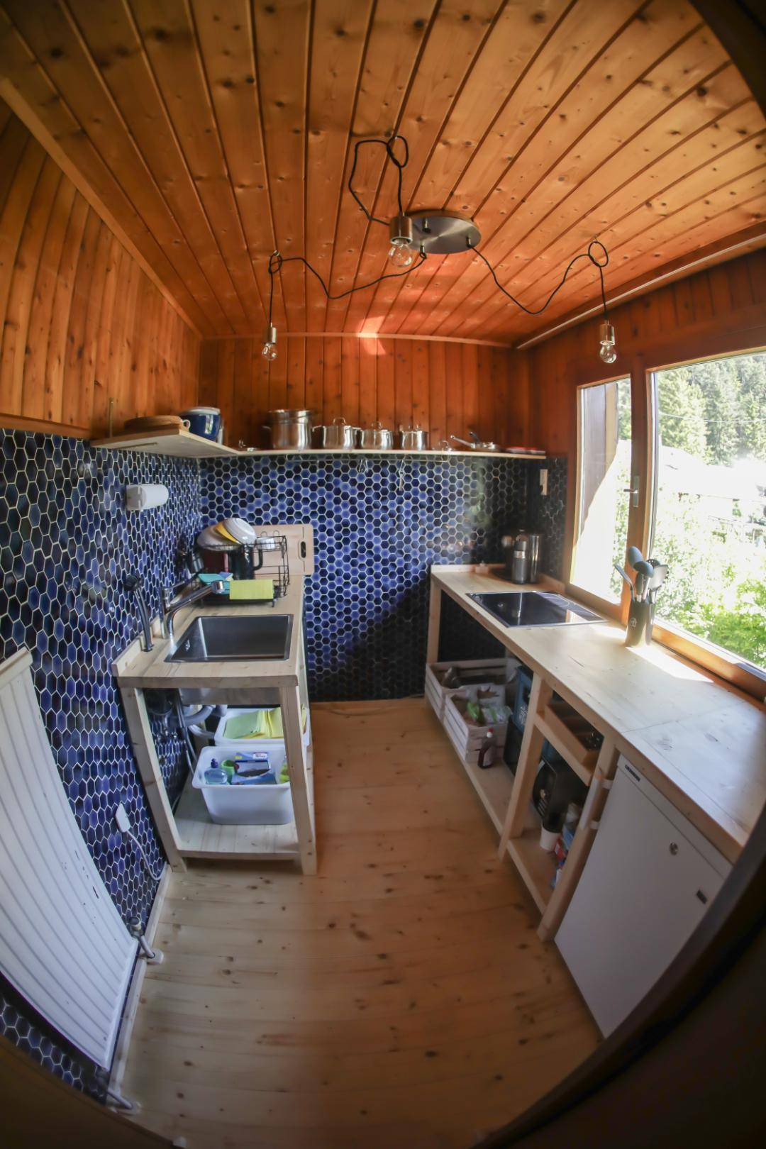 Rustikale Küche mit Holztheken, blauen Fliesen und Blick ins Grüne.