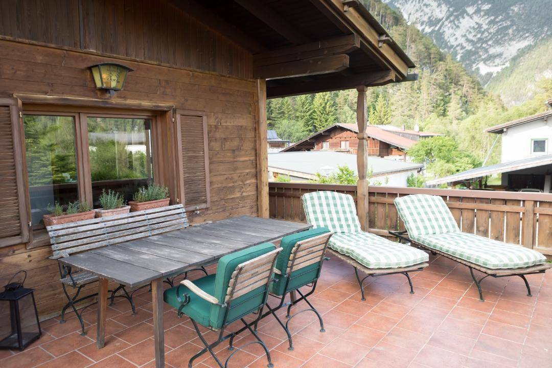 Geräumige Terrasse mit Liegestühlen und Esstisch, umgeben von Bergen und Natur.