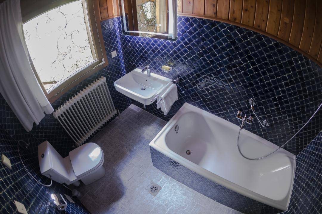 Badezimmer mit blauen Mosaikfliesen, Badewanne, Waschbecken und Toilette.