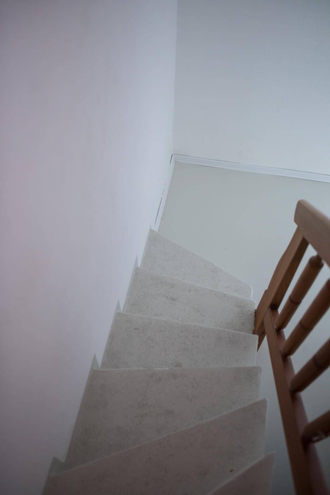 Schlichtes Treppenhaus mit weiß gestrichenen Wänden und Holzgeländer.