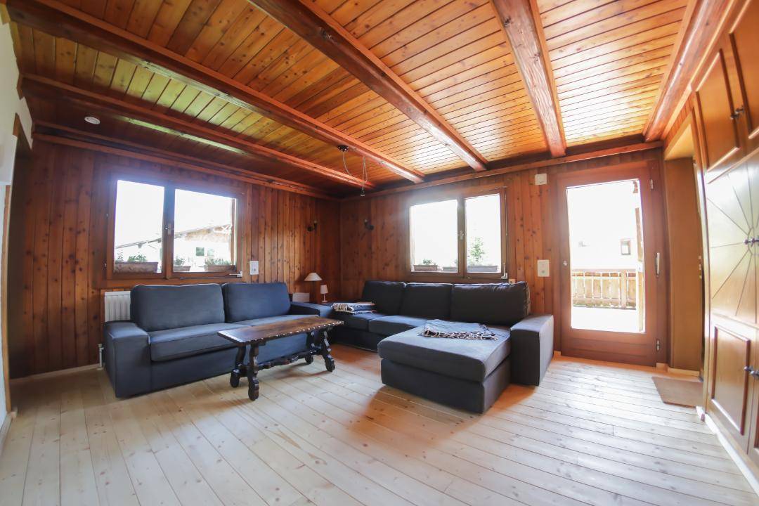 Geräumiges Wohnzimmer im alpinen Stil mit Holzvertäfelung, Sofas und Zugang zur Terrasse.