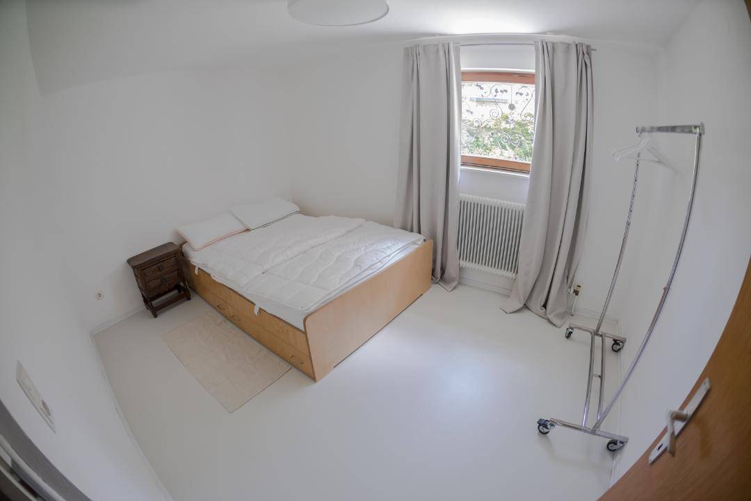 Helles Schlafzimmer mit weiß gestrichenen Wänden, Holzbett und einem mobilen Kleiderständer.