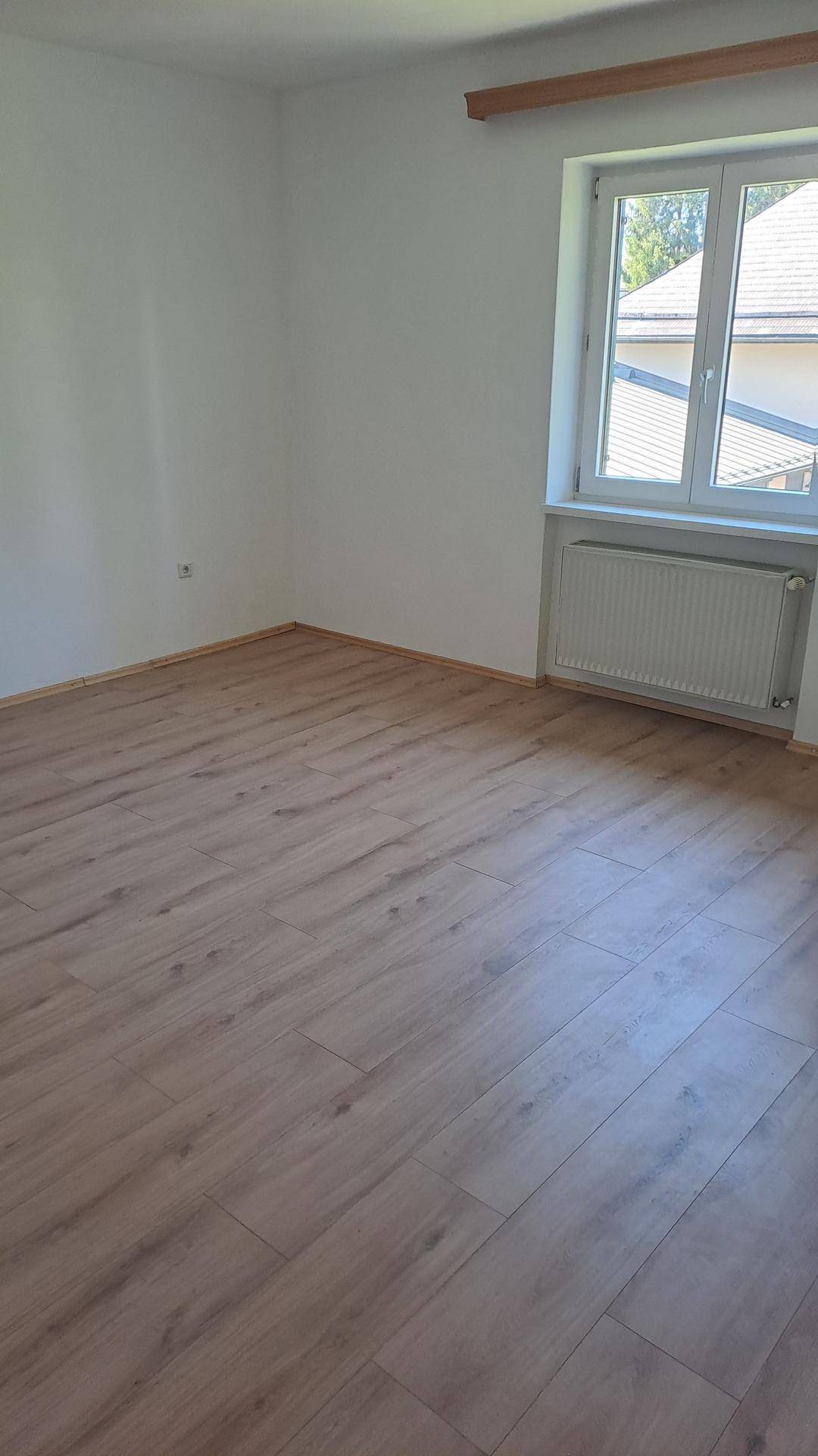 Helles Zimmer mit Laminatboden und Fenster, bereit zur individuellen Gestaltung.