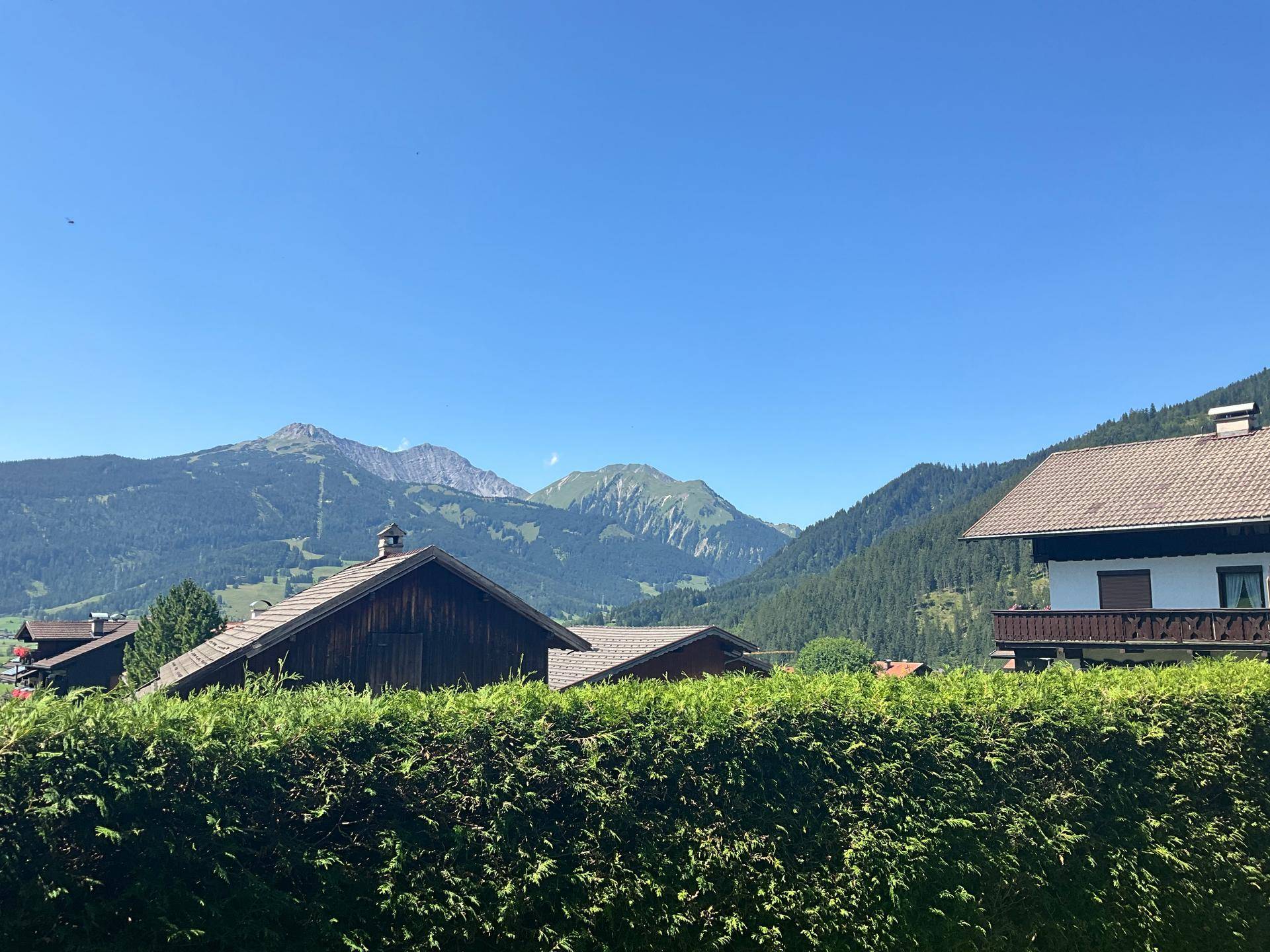 Idyllischer Blick auf traditionelle Häuser und grüne Berge unter einem klaren blauen Himmel.