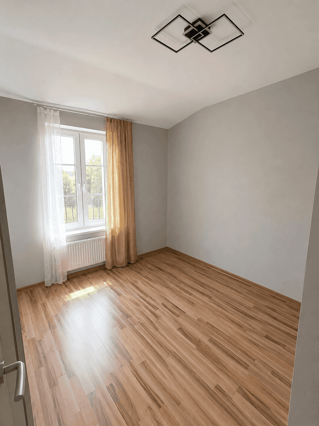 Schlafzimmer mit Holzboden, grauen Wänden und großem Fenster mit Blick ins Grüne.