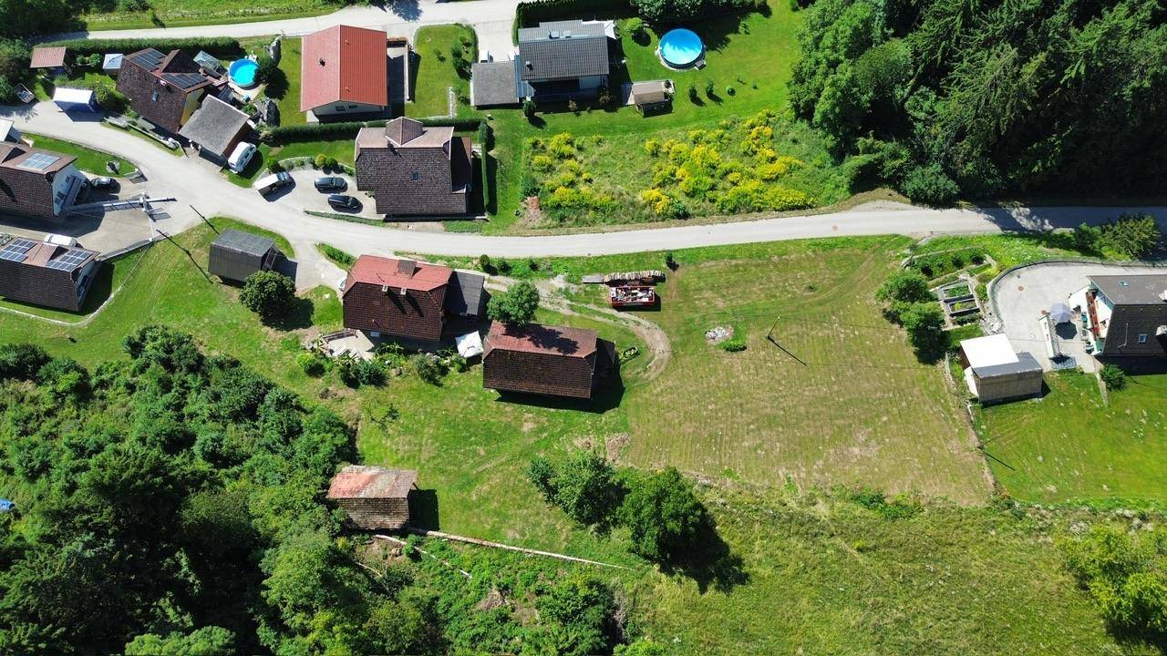 Vogelperspektive einer ländlichen Siedlung mit Feldern und Bergen im Hintergrund unter blauem Himmel.