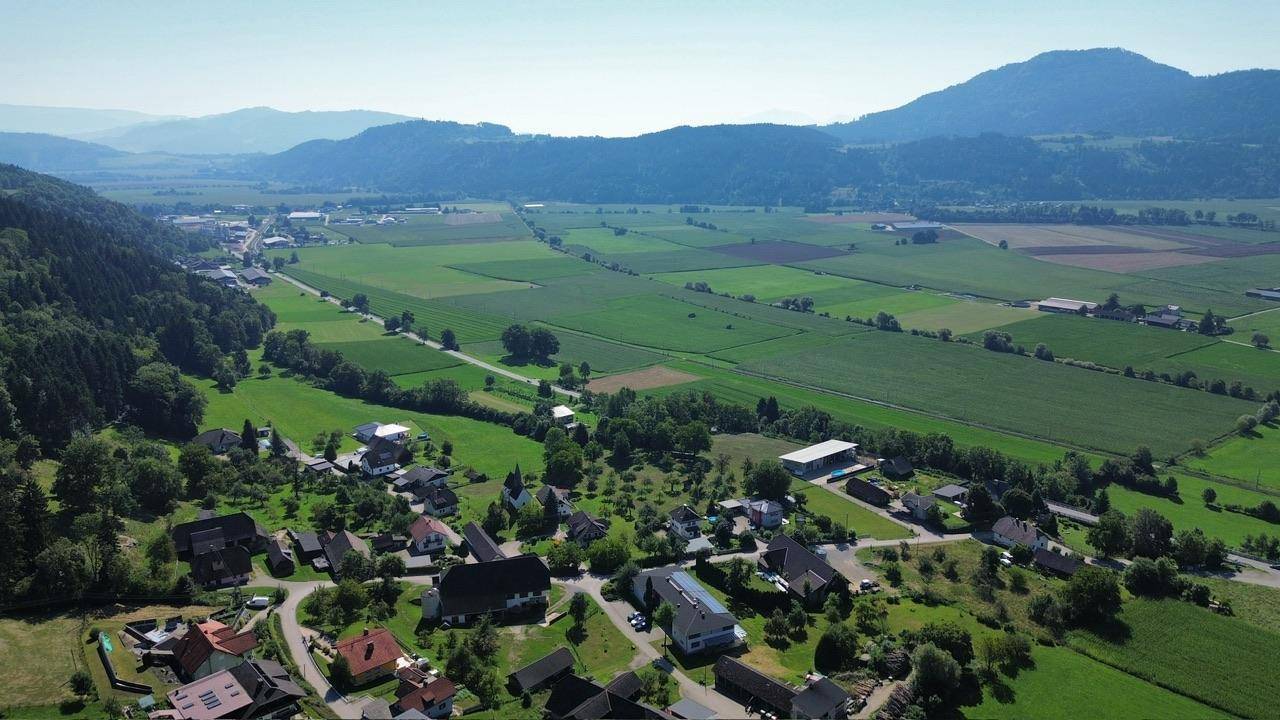 Weitläufiges Tal mit einem Dorf, grünen Feldern und majestätischen Bergen im Hintergrund.