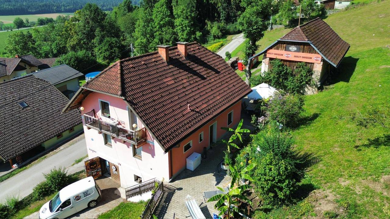 Wohnhaus mit mehreren Balkonen und gepflasterter Auffahrt, umgeben von grüner Landschaft.