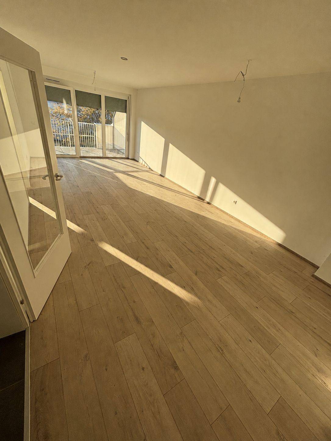 Heller Wohnbereich mit Holzboden, viel Tageslicht und Zugang zu einem Balkon.