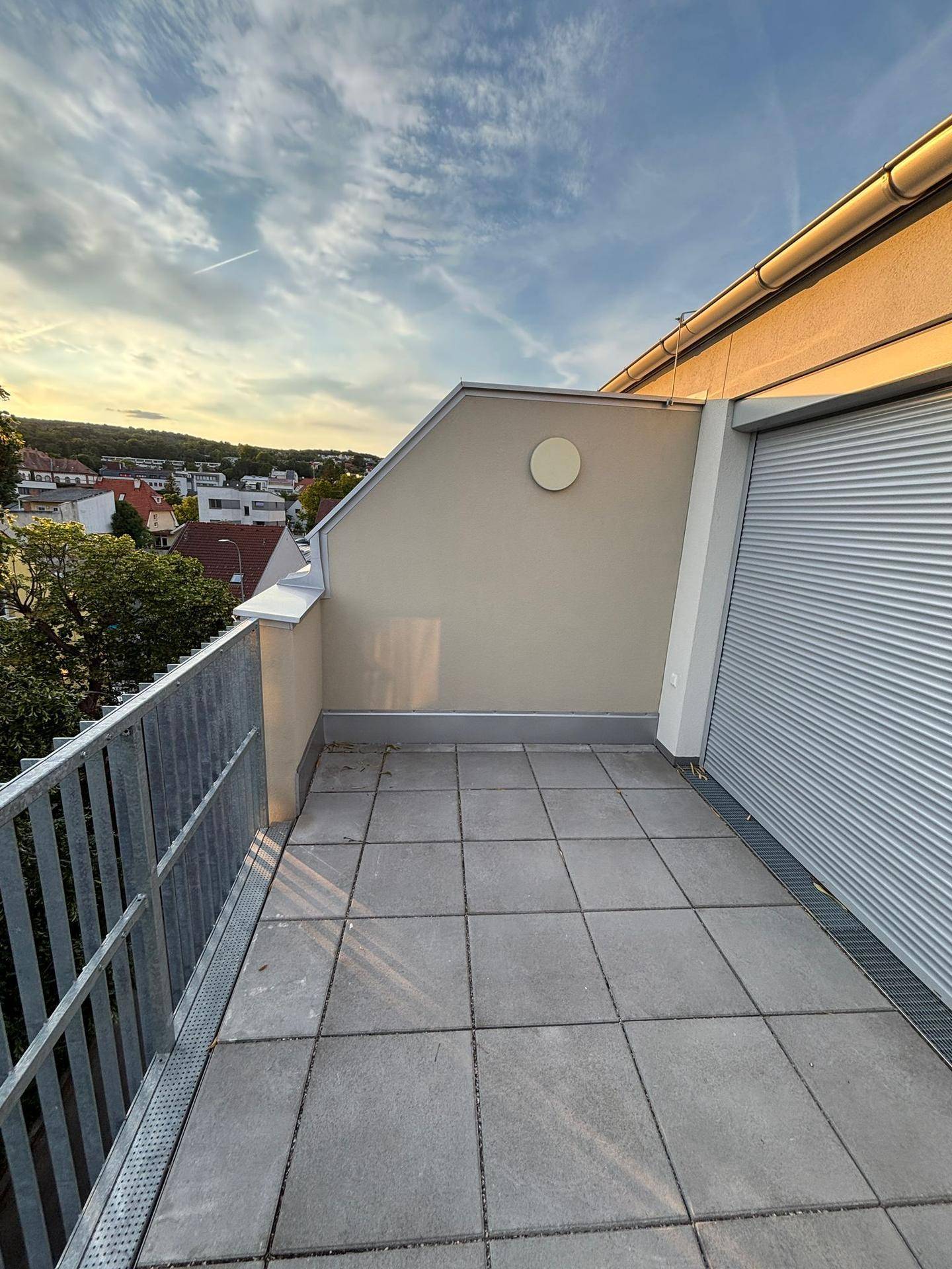 Balkon mit Fliesenboden und seitlichem Blick auf die Dächer und Bäume der Umgebung.