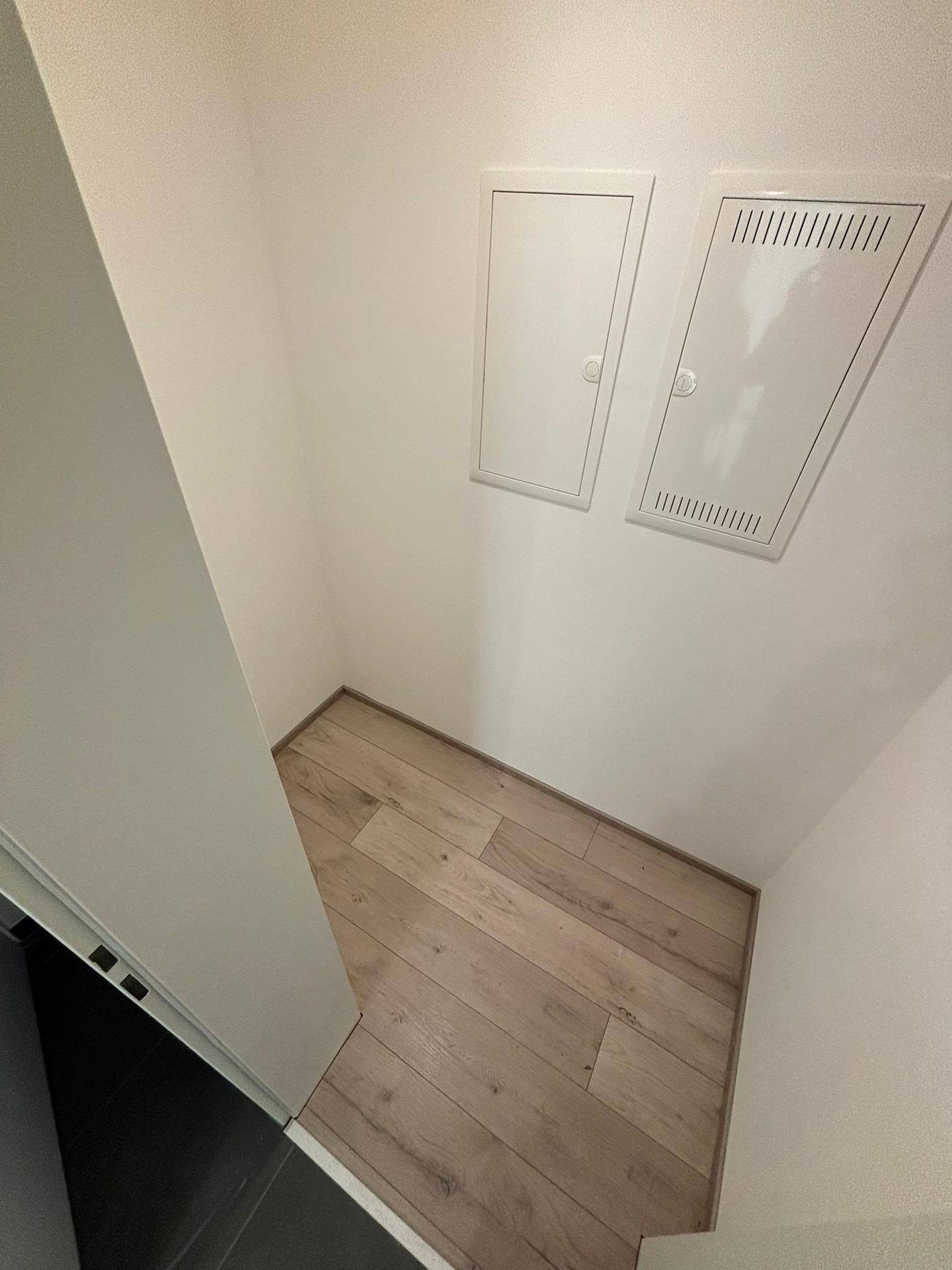 Kleiner Abstellraum mit hellem Laminatboden und Zugangsklappen an der Wand.