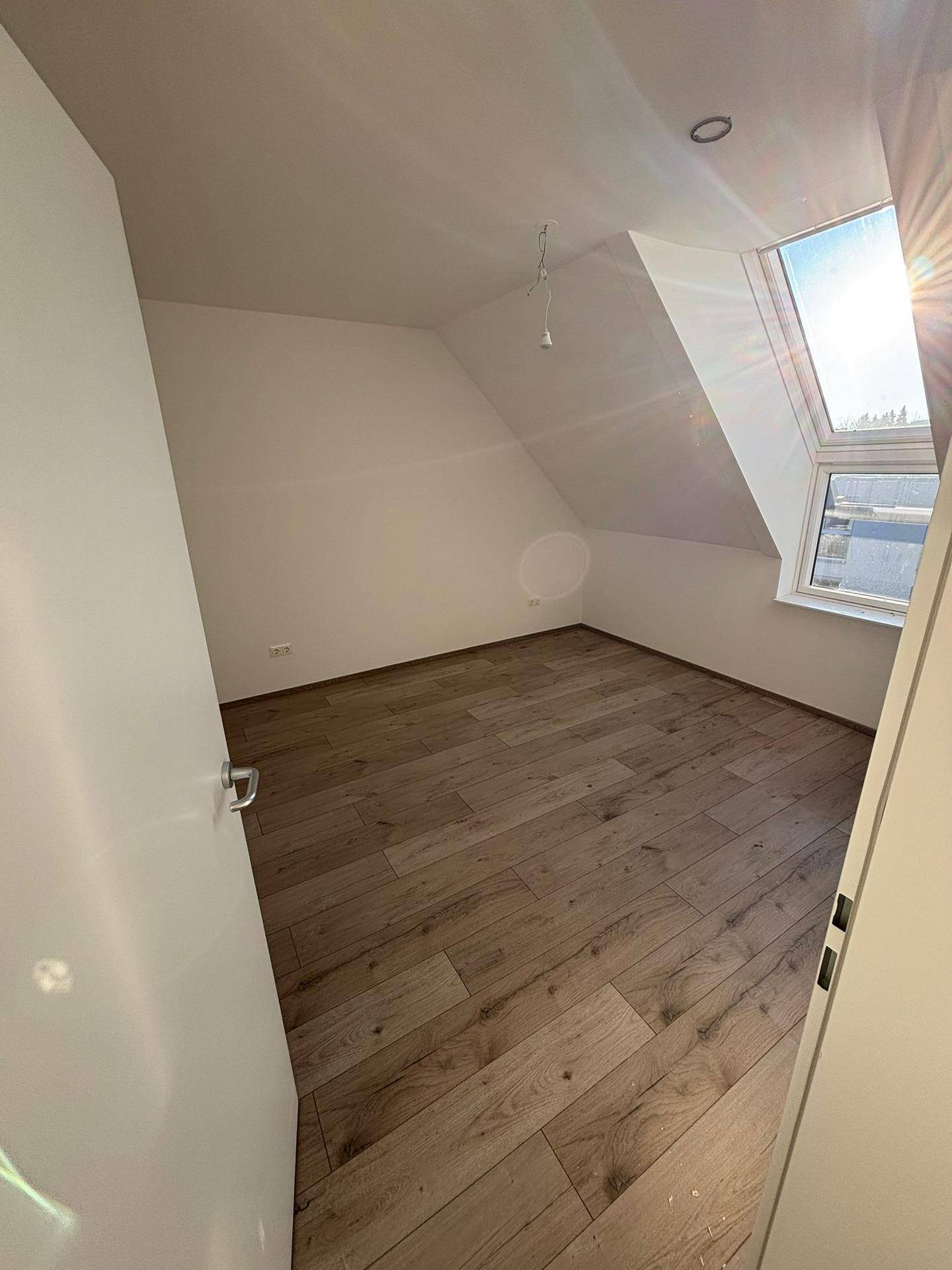 Schlafzimmer im Dachgeschoss mit schrägen Wänden, Holzboden und Dachfenster für viel Licht.