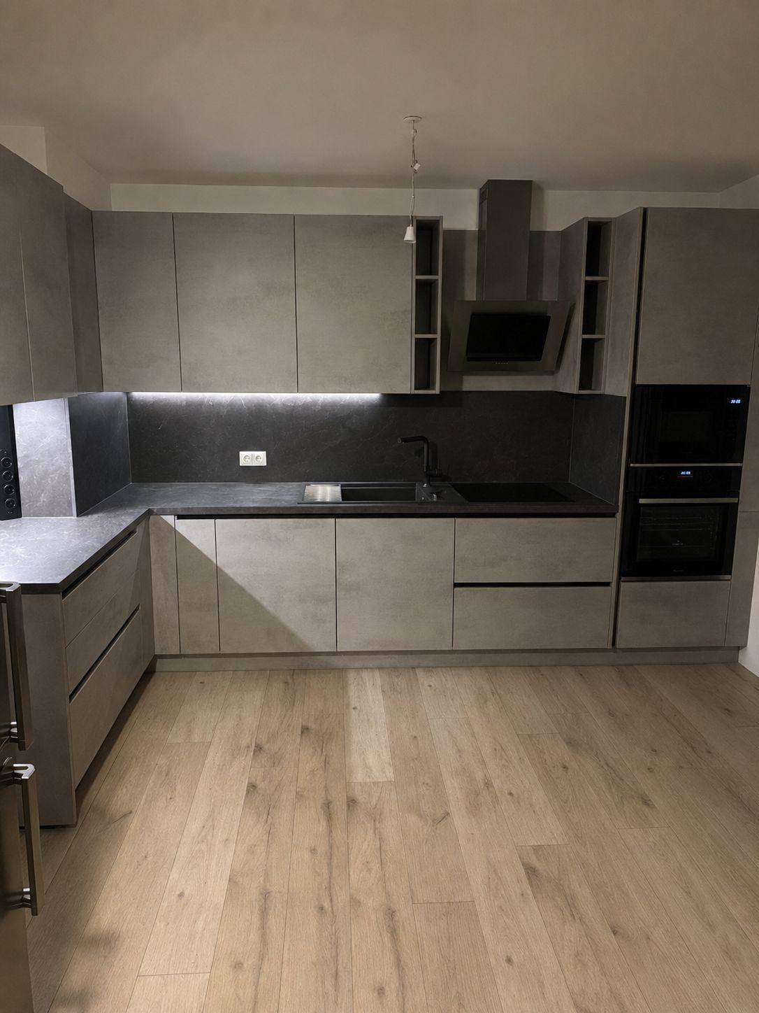 Moderne Einbauküche in Grau mit integrierten Geräten und hellem Holzboden.