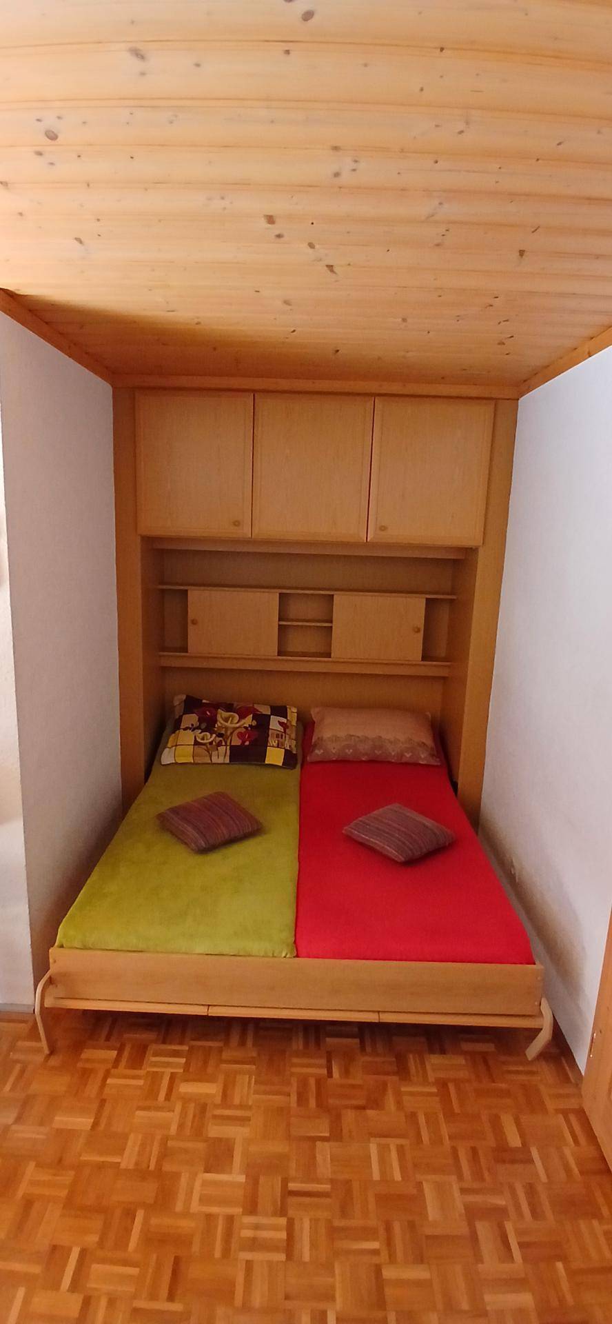Gemütliches Schlafzimmer mit eingebautem Bett, Holzvertäfelung an Decke und Wänden sowie farbigen Bettdecken.