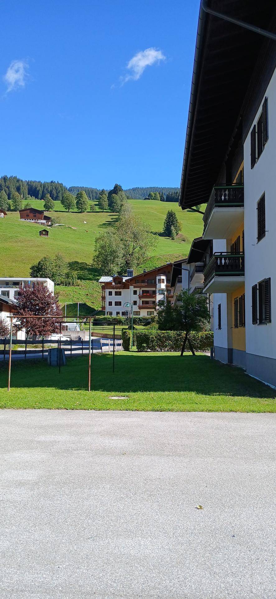 Gebäude mit Balkonen und weitem Blick auf grüne Hügel und weitere Häuser unter blauem Himmel.