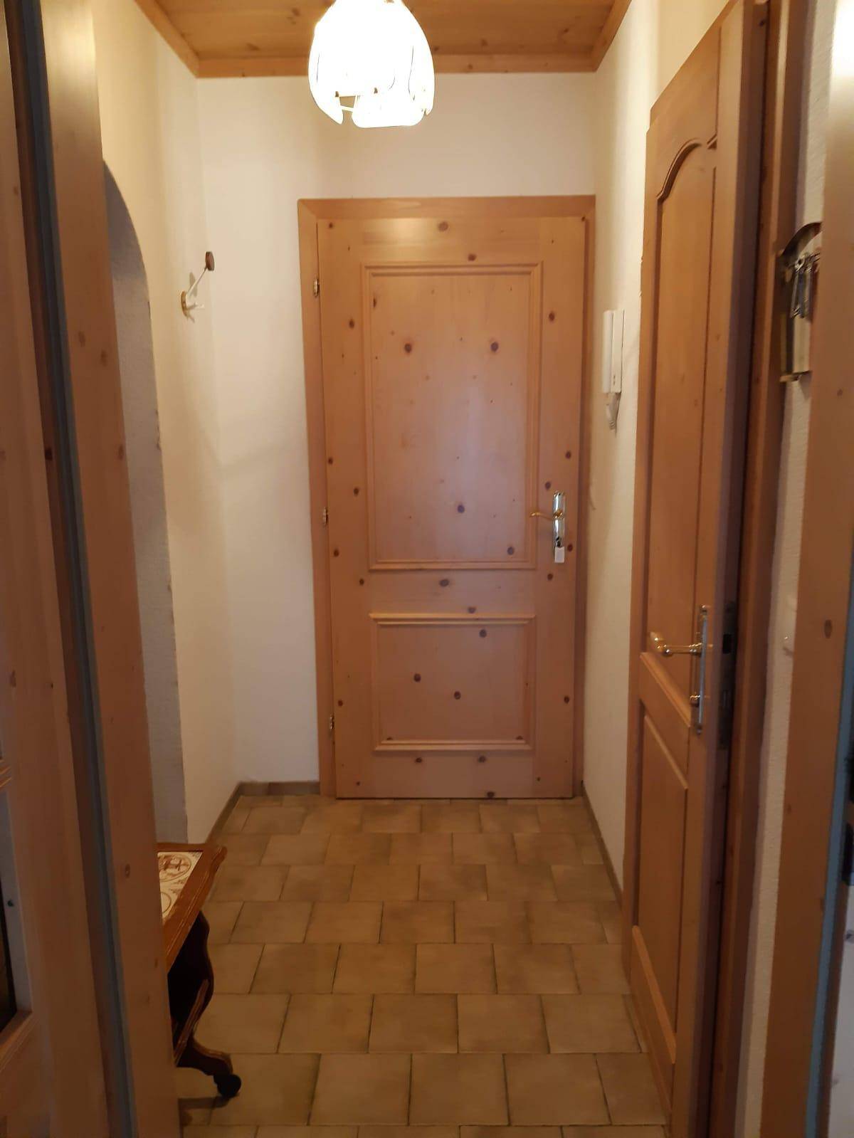 Heller Flur mit Holztüren, gefliestem Boden und einer warmen Deckenbeleuchtung.