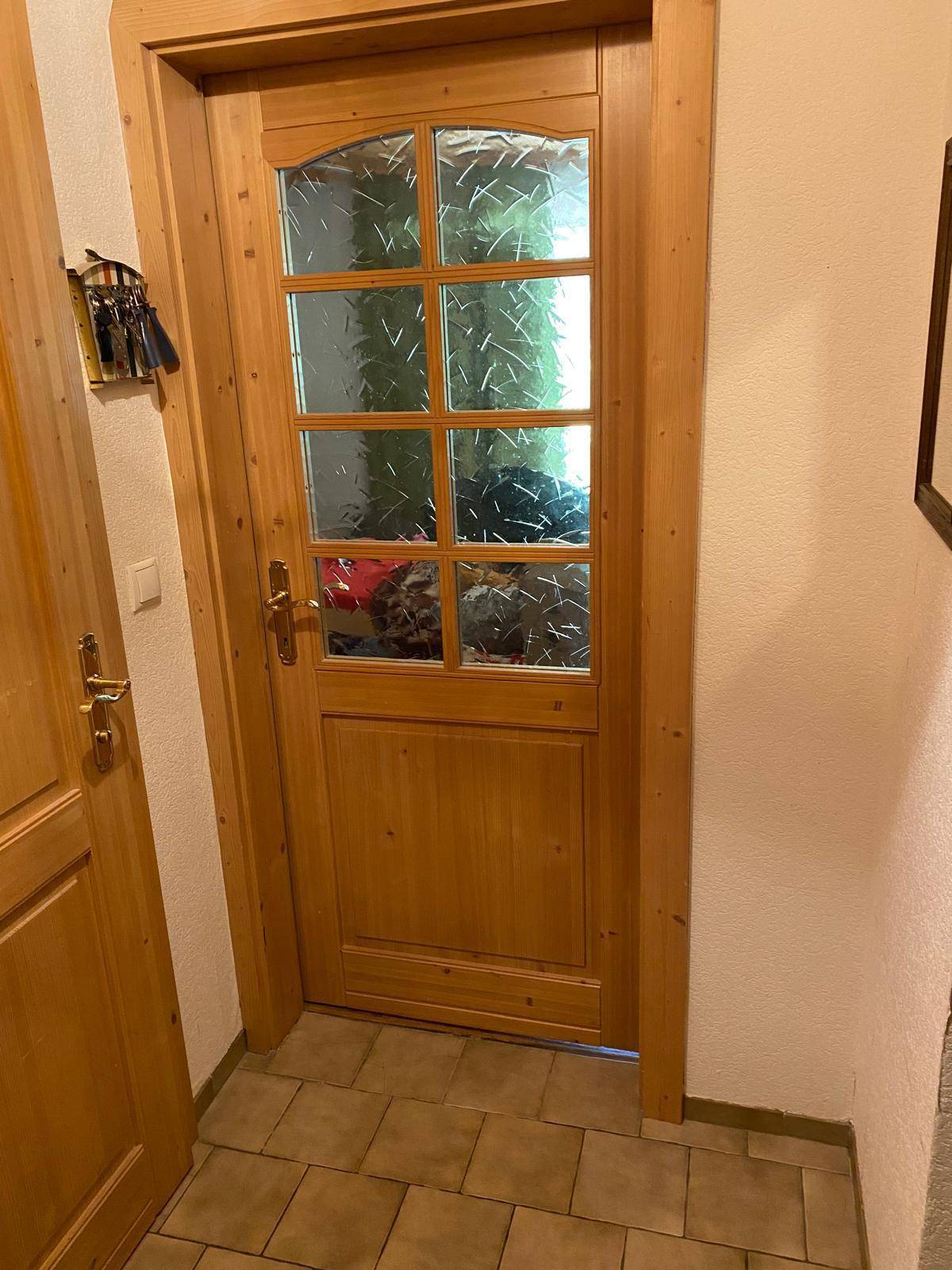 Holztür mit Glaseinsätzen und Fliesenboden in einem Flur, der zu einem weiteren Raum führt.
