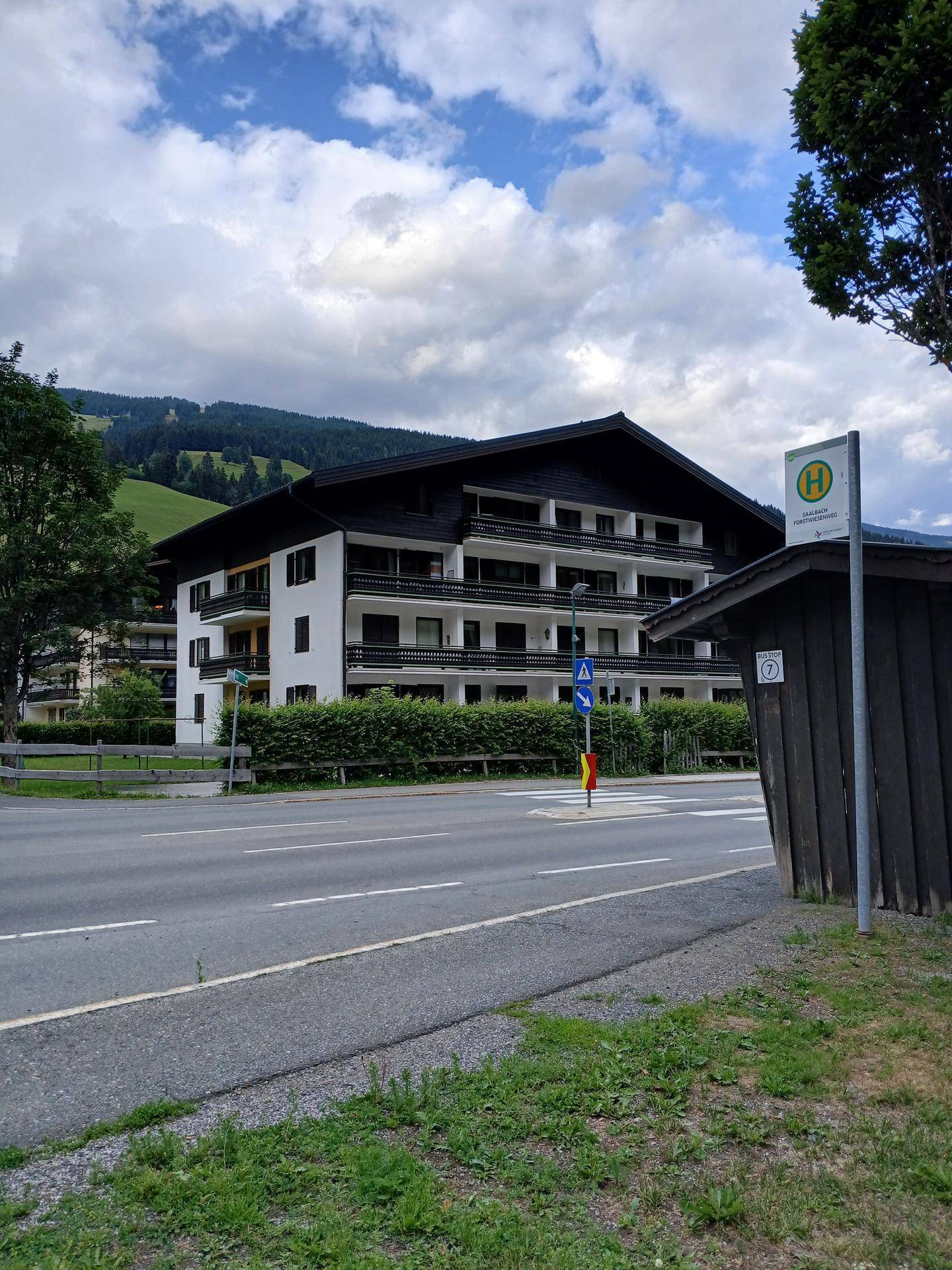 Mehrstöckiges Gebäude im alpinen Stil mit Balkonen und Blick auf die grünen Hügel.