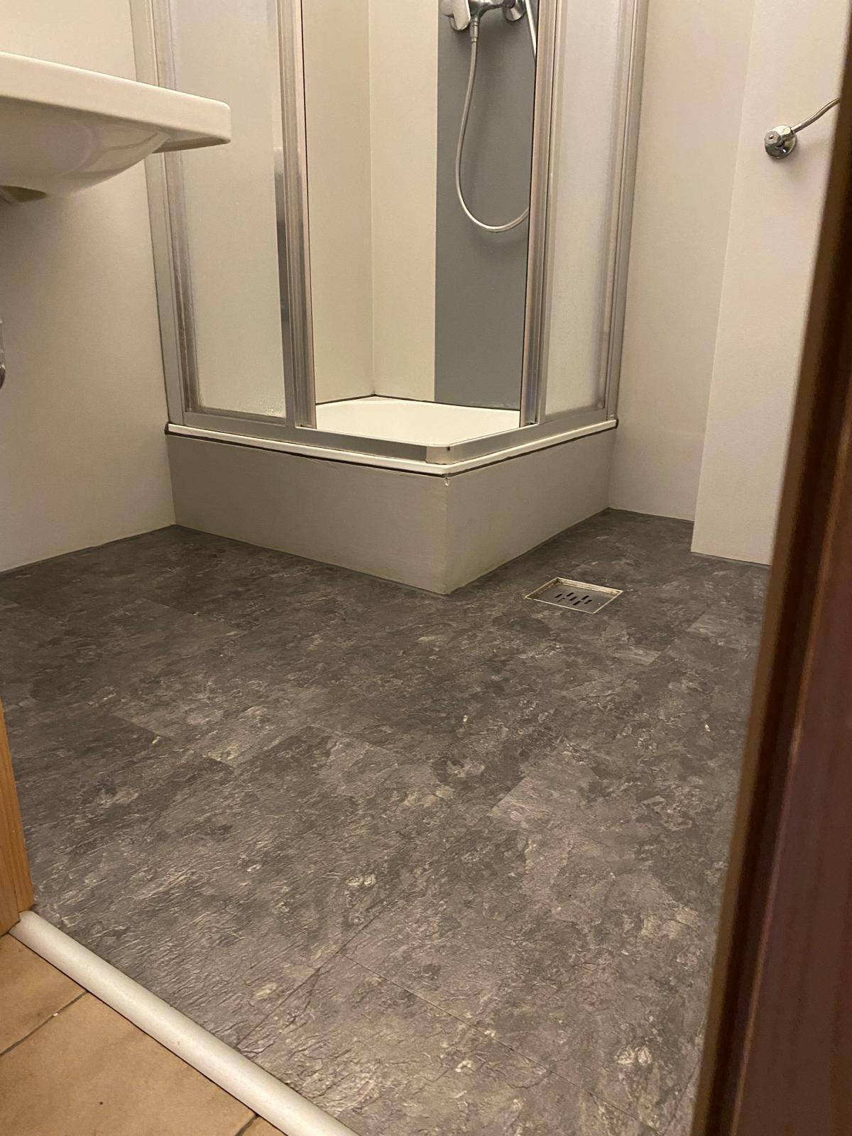 Badezimmer mit grauen Fliesen und einer Duschkabine, die einen funktionalen Bereich bietet.