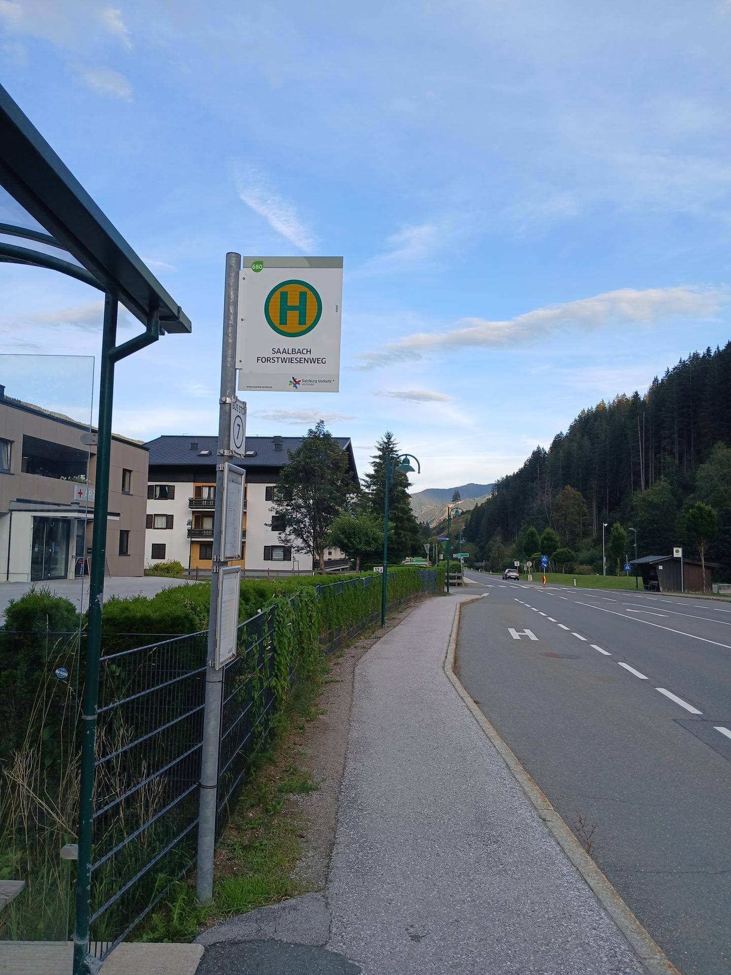 Bushaltestelle an einer Straße mit Blick auf die umliegende Berglandschaft und Bäume.