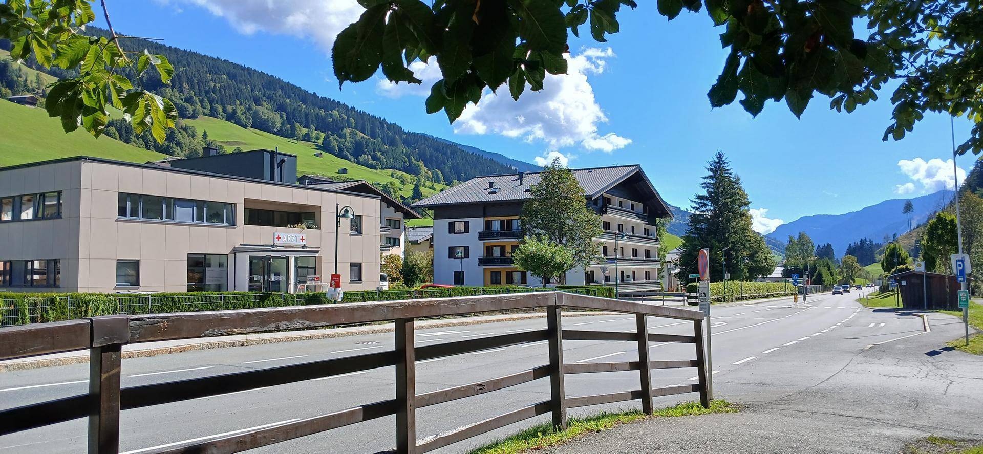 Mehrere Gebäude entlang einer Straße mit Blick auf eine weite grüne Berglandschaft.