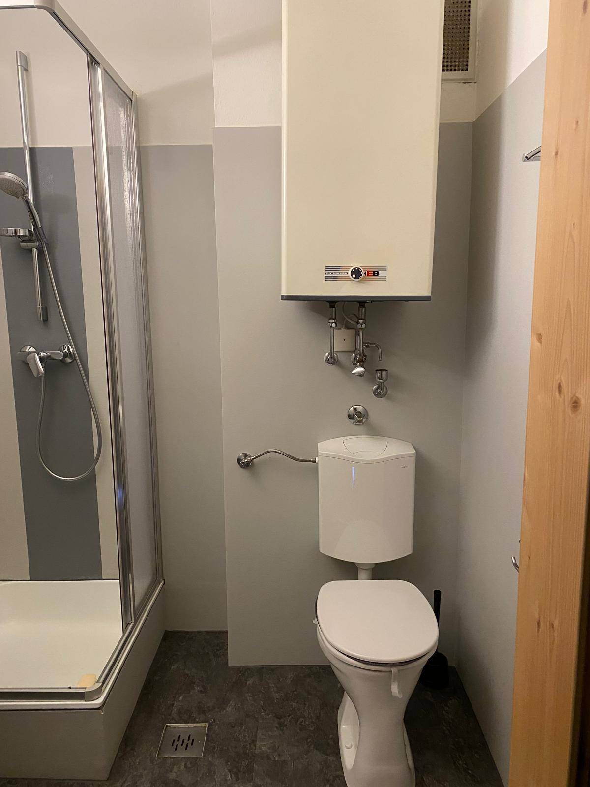 Badezimmer mit Toilette, Duschkabine und einem an der Wand montierten Warmwasserbereiter.