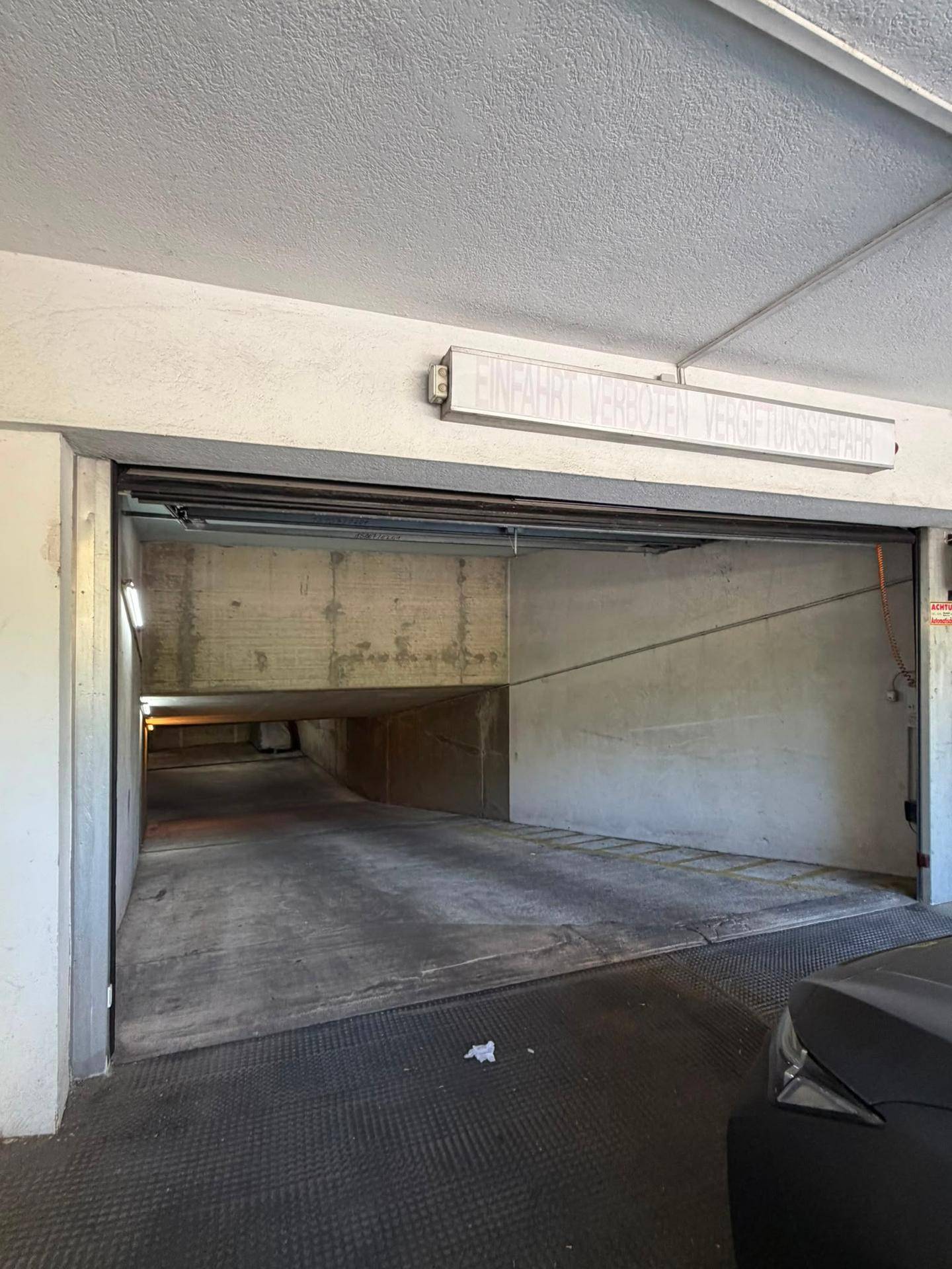 Einfahrt zu einer Tiefgarage mit Warnhinweis und Rampe, die in den unterirdischen Bereich führt.